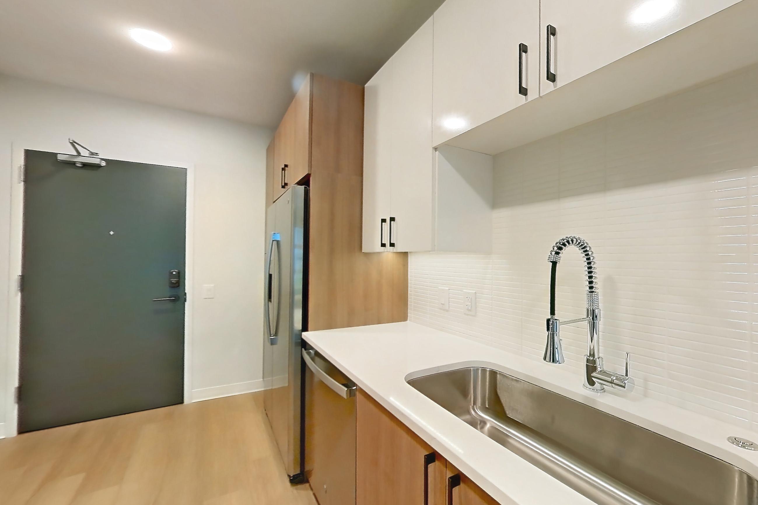 Kitchen with dishwasher, electric range, light countertops, light stone countertops, light wood-finish flooring, microwave, oven/range, refrigerator, and stainless steel appliances, Apartment 0332 at The Alcott