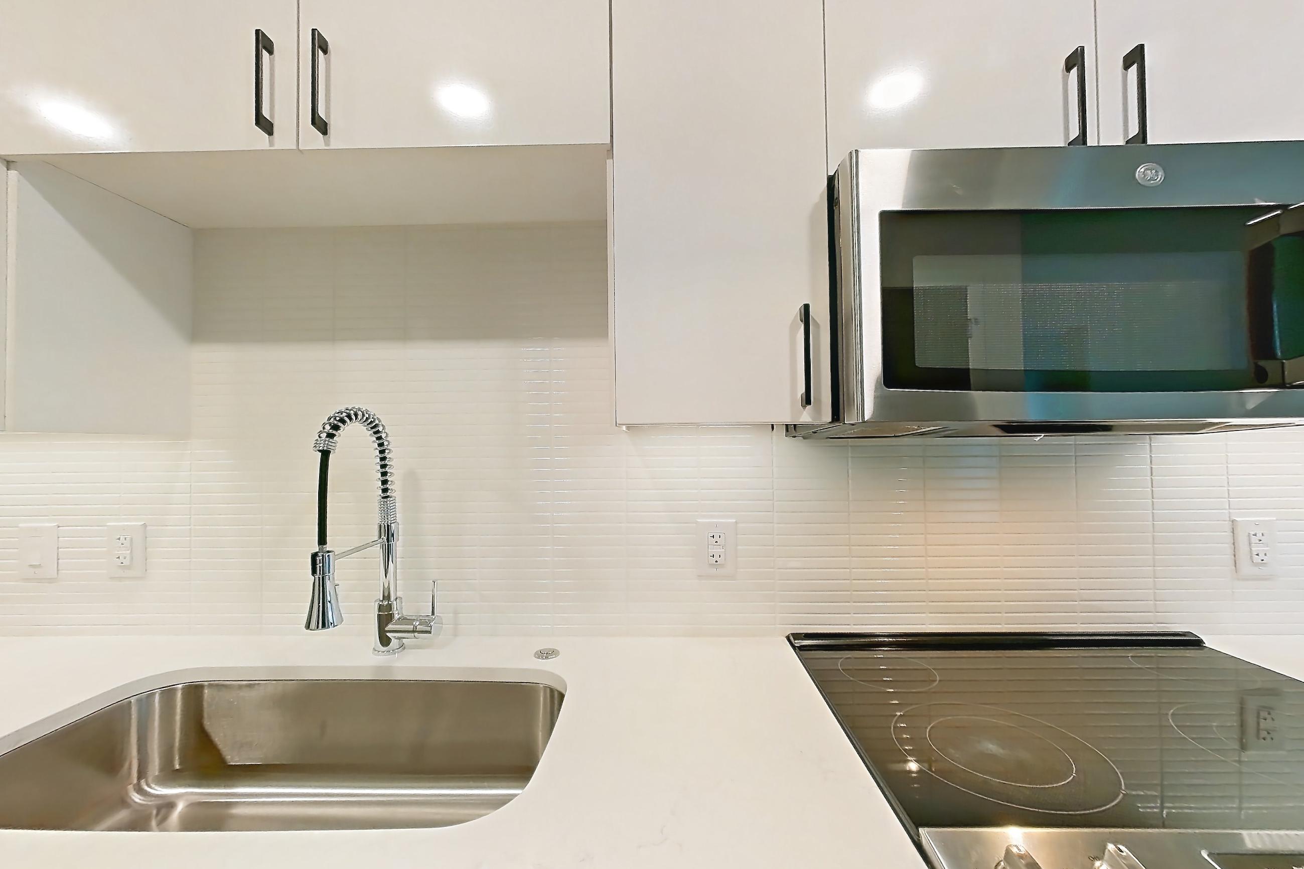 Kitchen with dishwasher, electric range, light countertops, light stone countertops, light wood-finish flooring, microwave, oven/range, refrigerator, and stainless steel appliances, Apartment 0332 at The Alcott