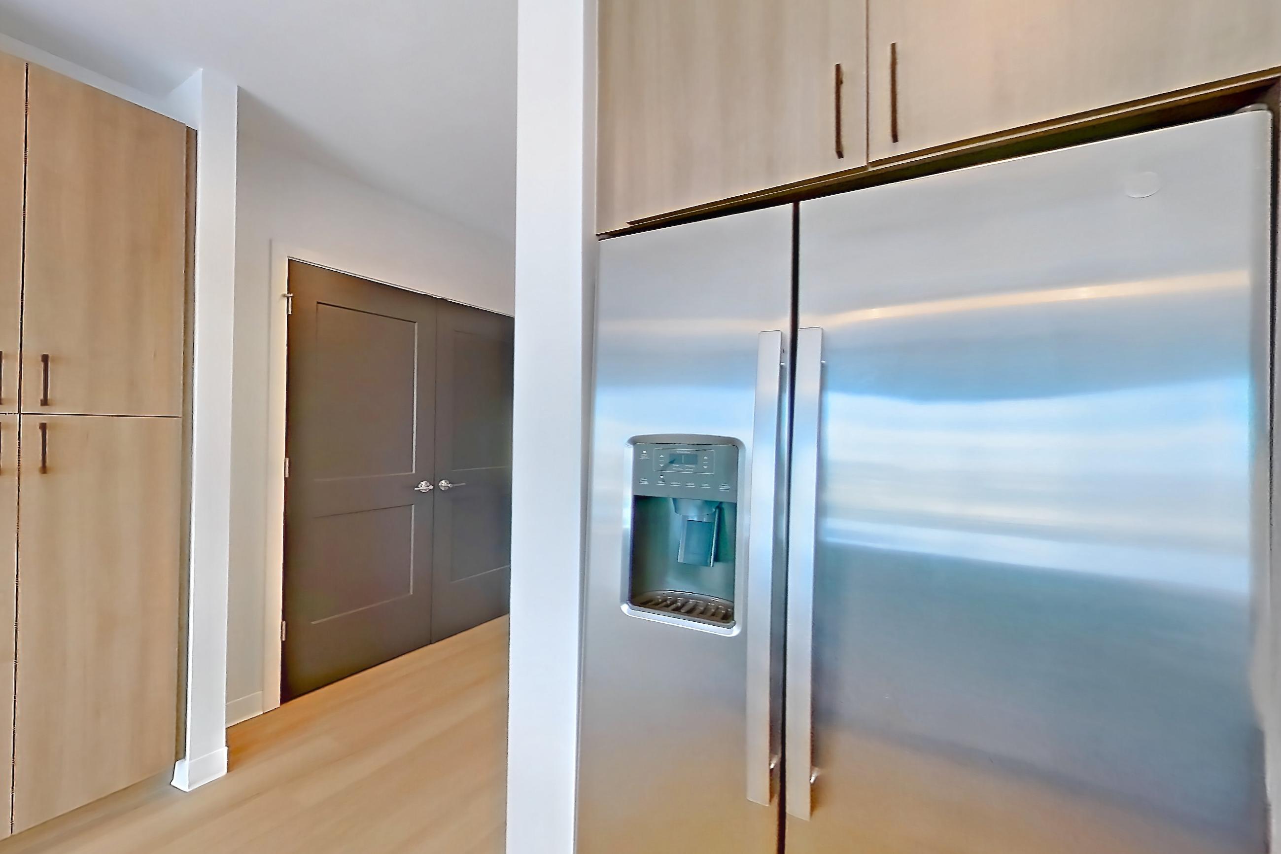 Kitchen with dishwasher, electric range, light countertops, light stone countertops, light wood-finish flooring, microwave, oven/range, refrigerator, stainless steel appliances, and water & ice dispenser, Apartment 1211 at The Alcott