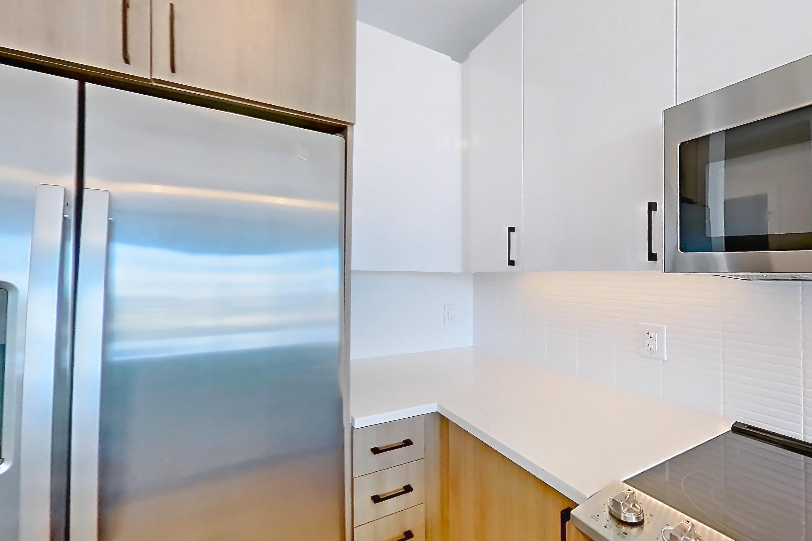 Kitchen with dishwasher, electric range, light countertops, light stone countertops, light wood-finish flooring, microwave, oven/range, refrigerator, stainless steel appliances, and water & ice dispenser, Apartment 1211 at The Alcott