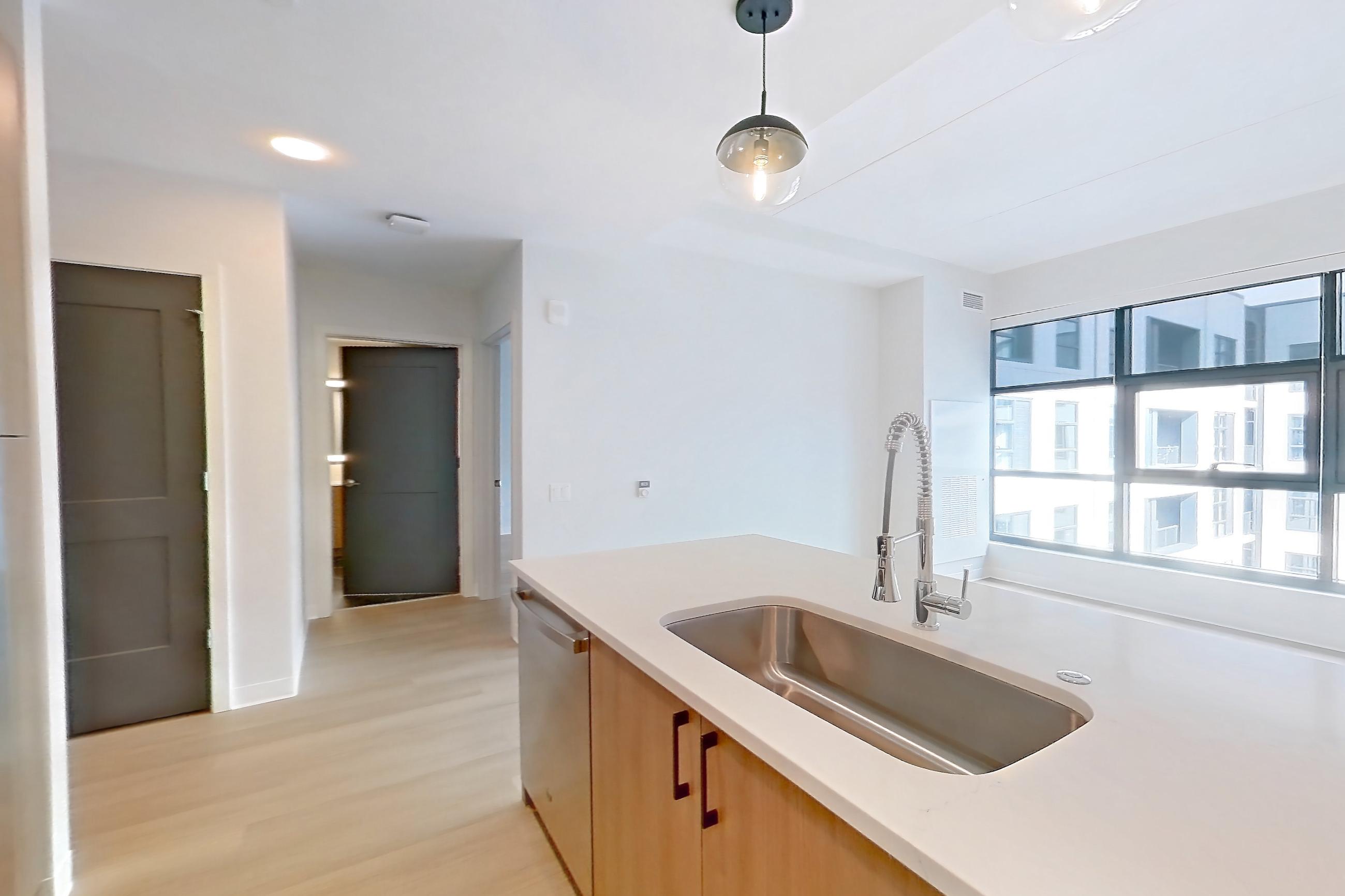 Kitchen with dishwasher, electric range, light countertops, light stone countertops, light wood-finish flooring, microwave, oven/range, refrigerator, stainless steel appliances, and water & ice dispenser, Apartment 1110 at The Alcott