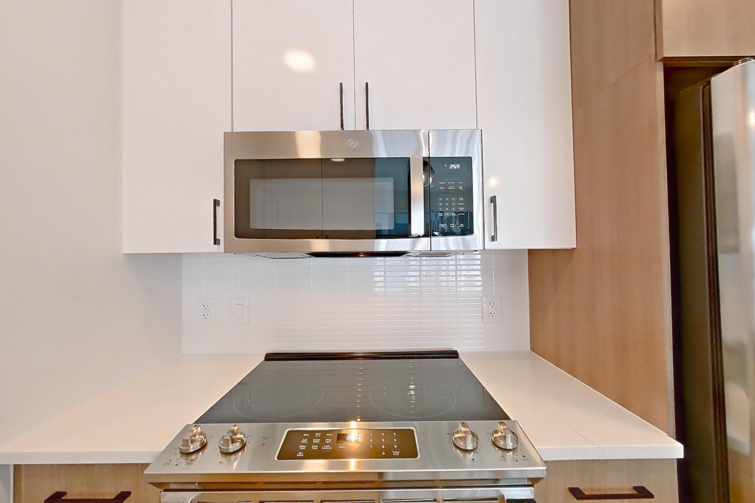 Kitchen with dishwasher, electric range, light countertops, light stone countertops, light wood-finish flooring, microwave, oven/range, refrigerator, stainless steel appliances, and water & ice dispenser, Apartment 1110 at The Alcott