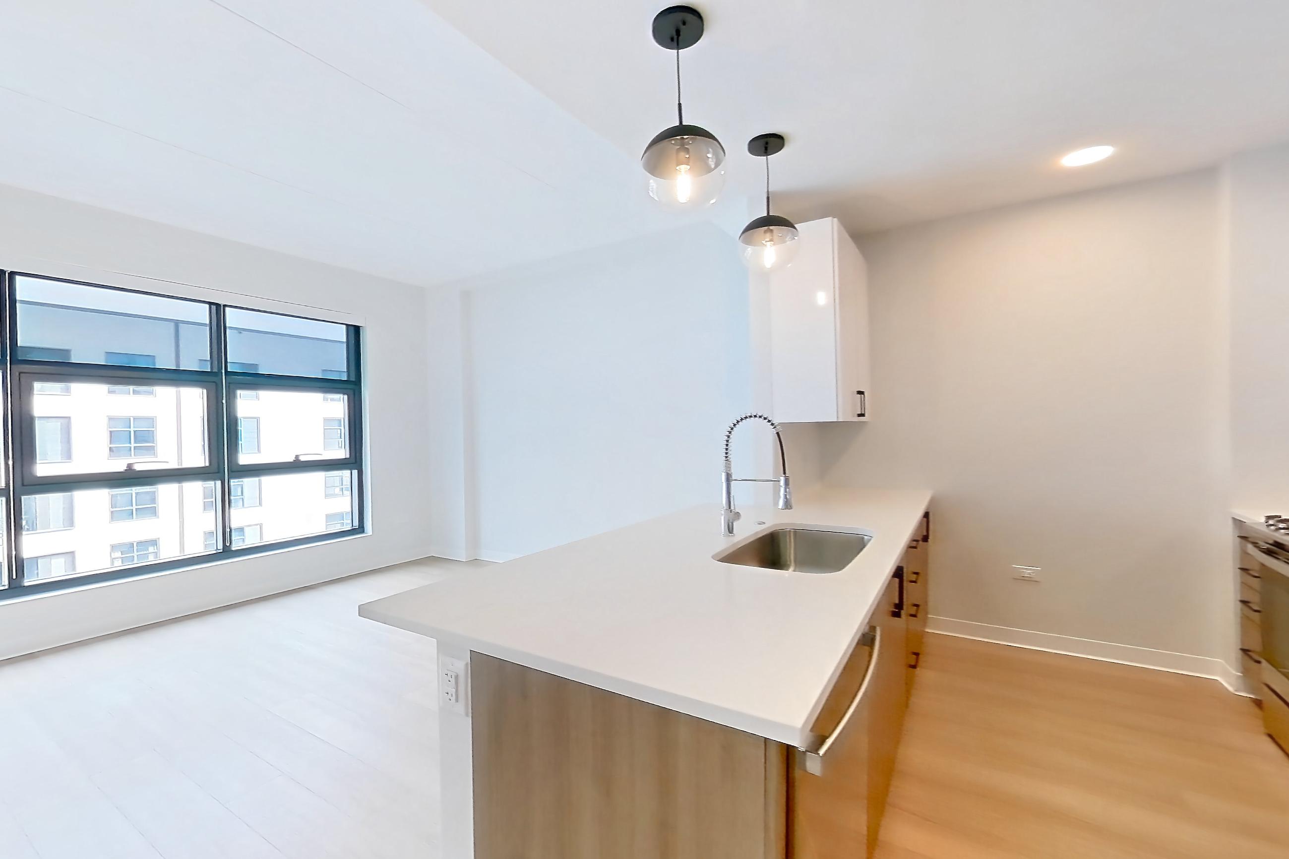 Living space with dishwasher, light stone countertops, light wood-finish flooring, oven/range, refrigerator, and stainless steel appliances, Apartment 1110 at The Alcott