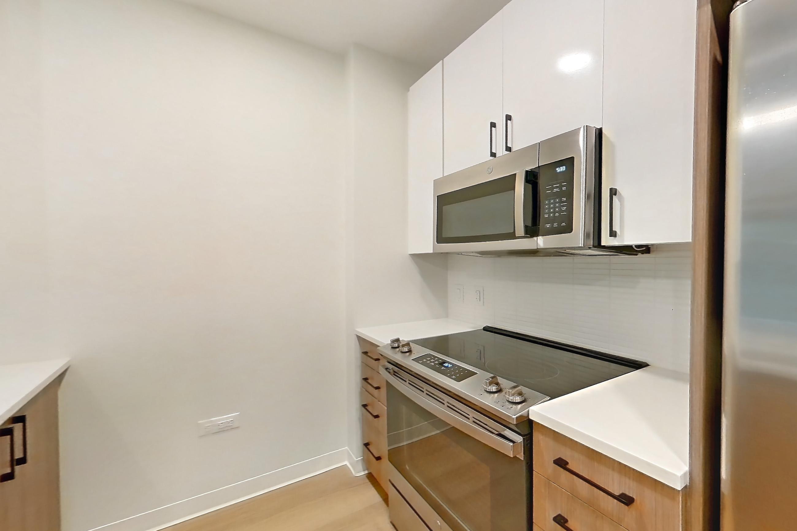 Kitchen with dishwasher, electric range, light countertops, light stone countertops, light wood-finish flooring, oven/range, and stainless steel appliances, Apartment 0210 at The Alcott