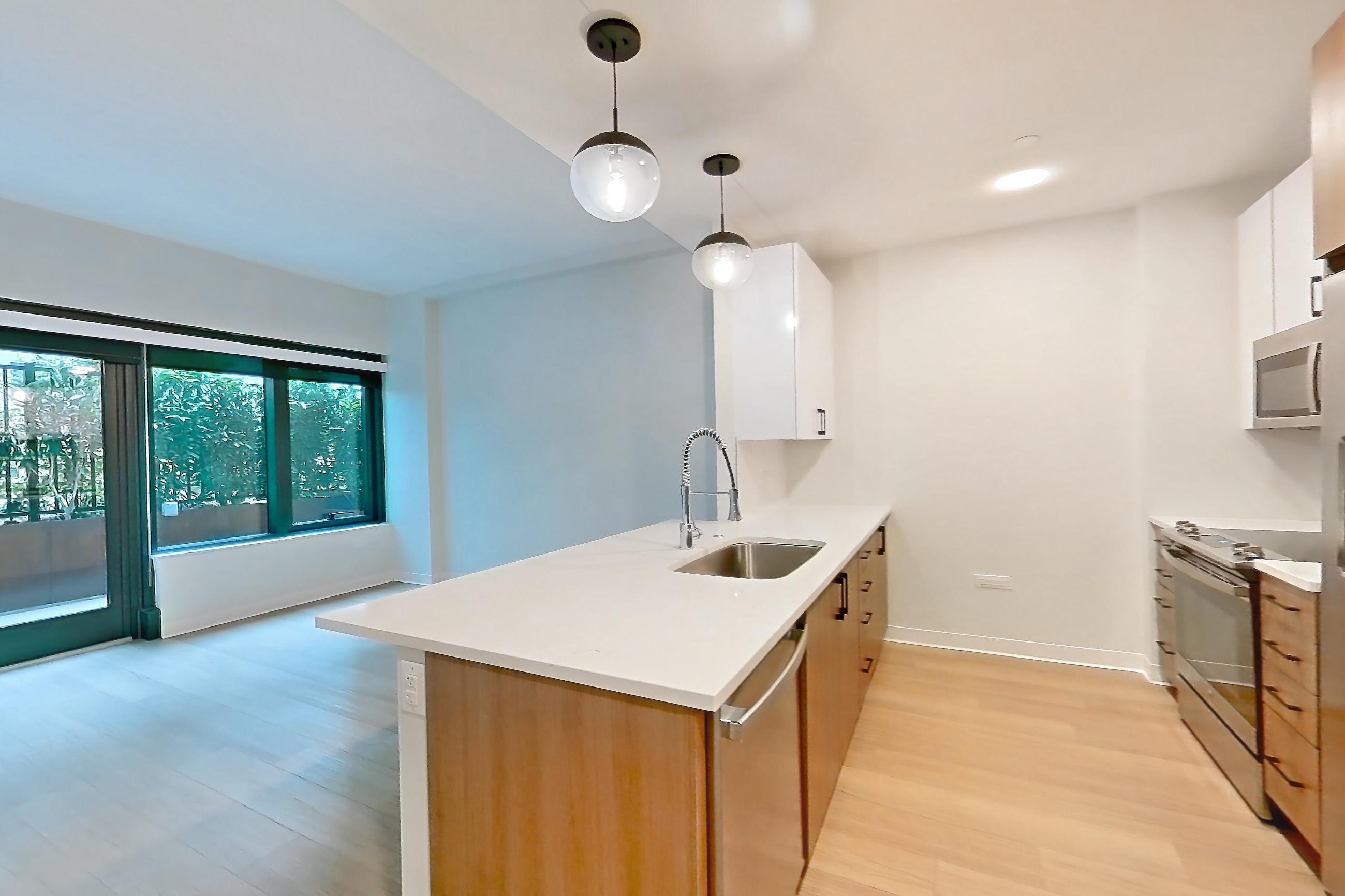 Living space with dishwasher, light countertops, light stone countertops, light wood-finish flooring, oven/range, refrigerator, and stainless steel appliances, Apartment 0210 at The Alcott