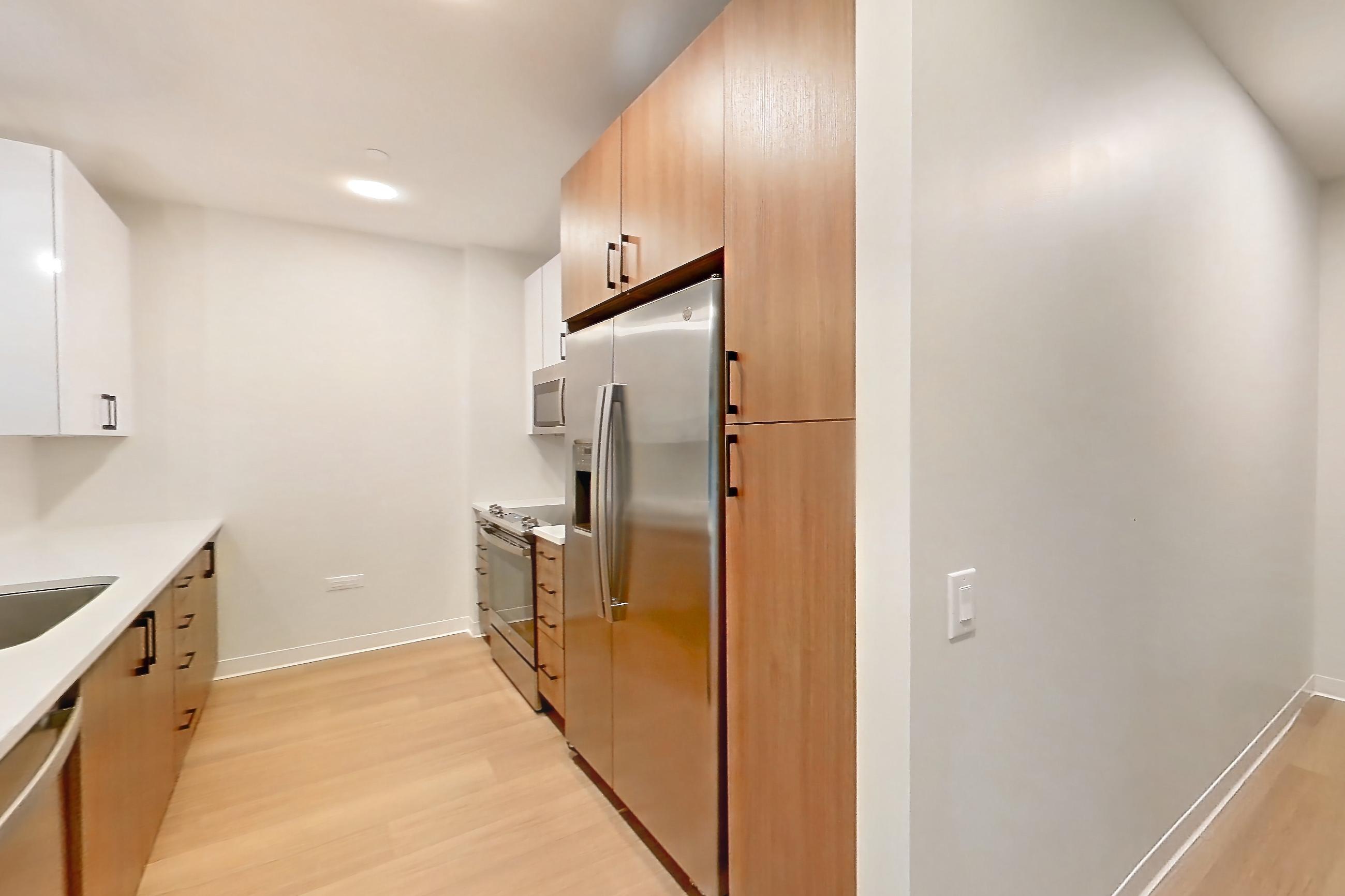 Living space with dishwasher, light countertops, light stone countertops, light wood-finish flooring, oven/range, refrigerator, and stainless steel appliances, Apartment 0210 at The Alcott