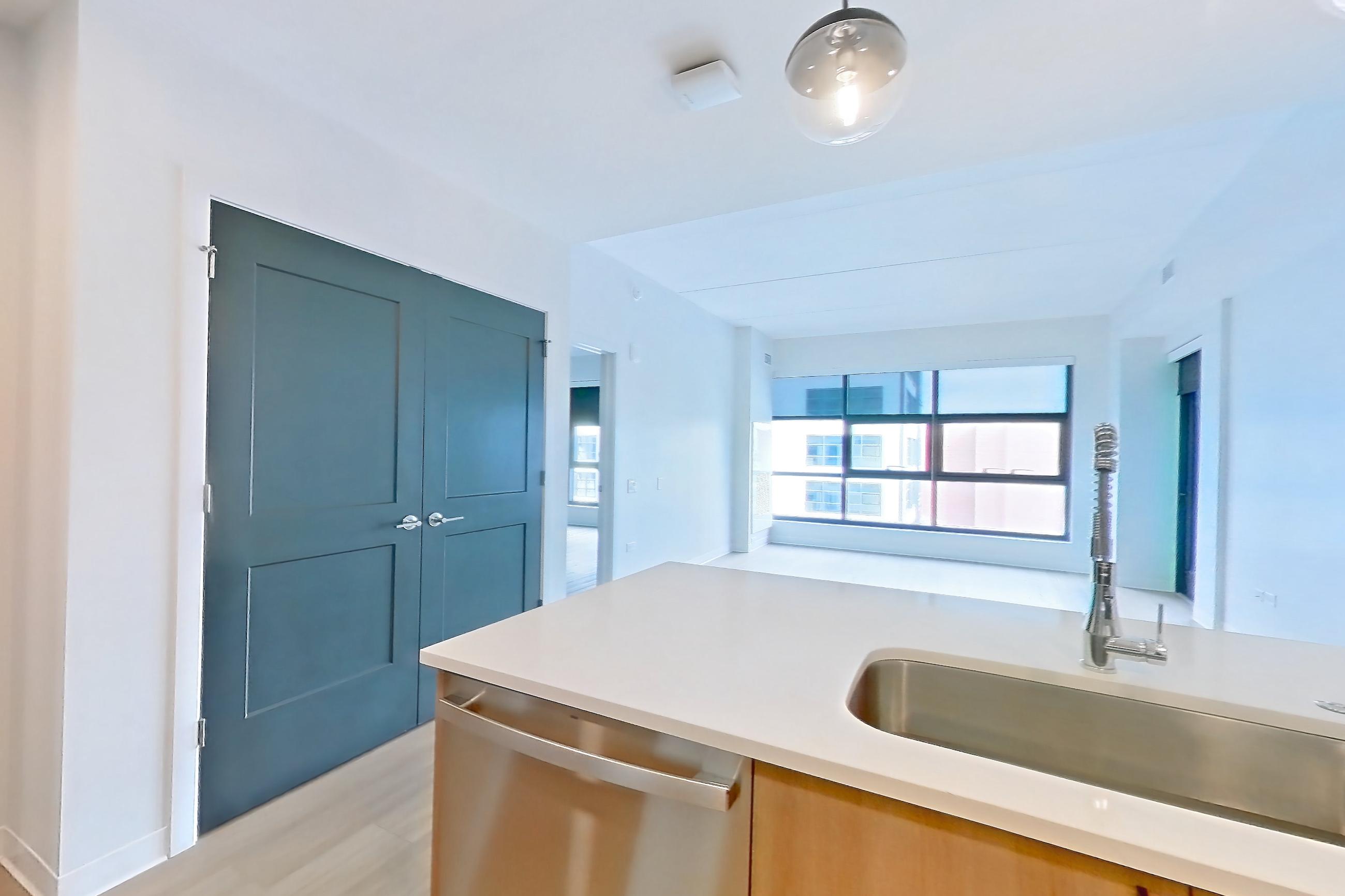 Kitchen with dishwasher, electric range, kitchen island, light countertops, light stone countertops, light wood-finish flooring, microwave, oven/range, refrigerator, stainless steel appliances, and water & ice dispenser, Apartment 0904 at The Alcott