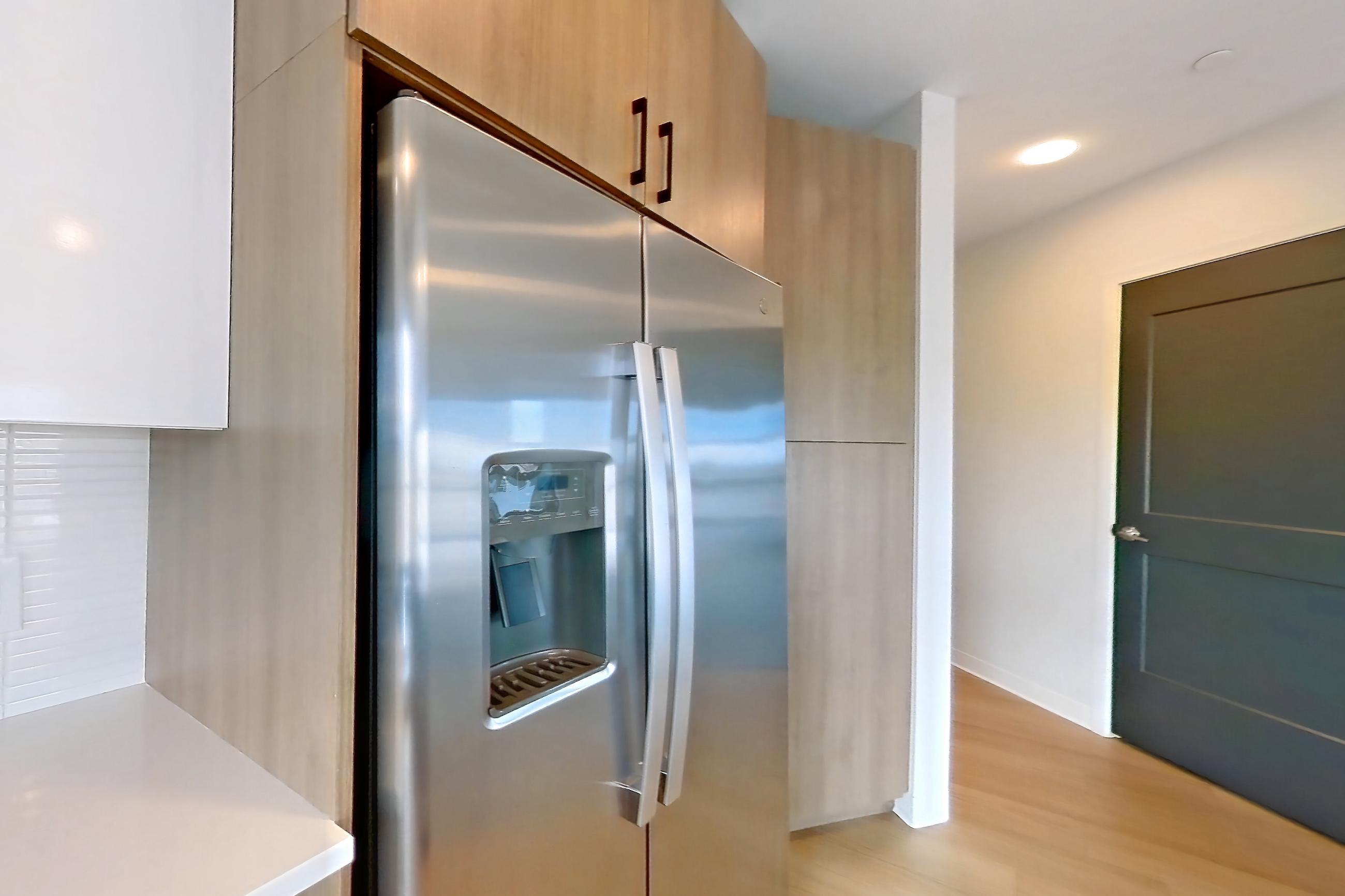 Kitchen with dishwasher, electric range, light countertops, light stone countertops, light wood-finish flooring, oven/range, refrigerator, stainless steel appliances, and water & ice dispenser, Apartment 0729 at The Alcott