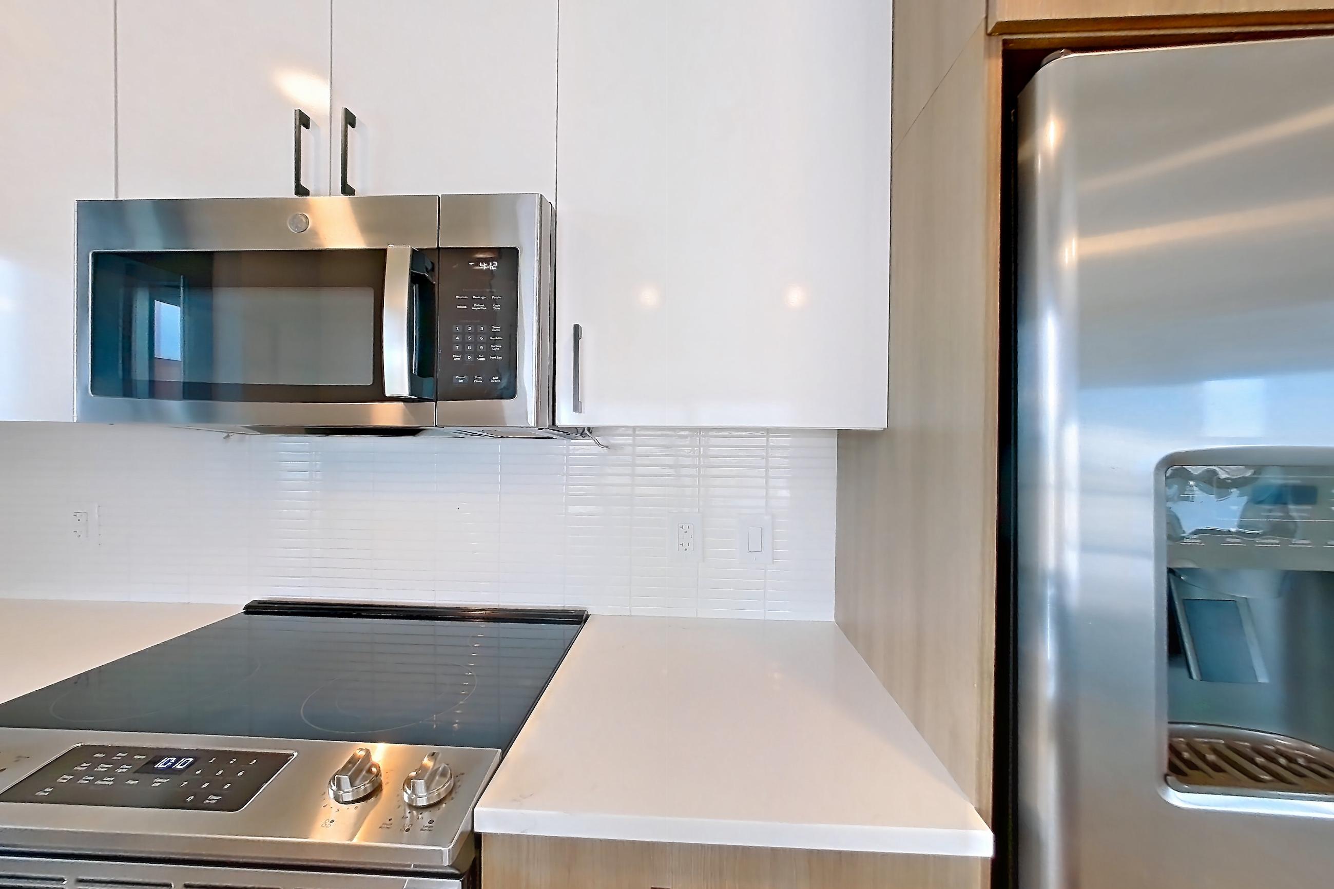 Kitchen with dishwasher, electric range, light countertops, light stone countertops, light wood-finish flooring, oven/range, refrigerator, stainless steel appliances, and water & ice dispenser, Apartment 0729 at The Alcott