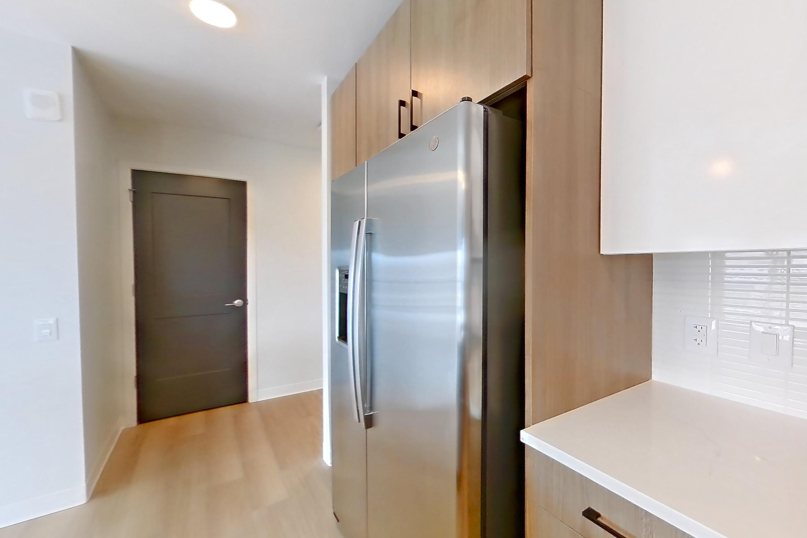 Kitchen with dishwasher, electric range, light countertops, light stone countertops, light wood-finish flooring, oven/range, refrigerator, and stainless steel appliances, Apartment 0702 at The Alcott