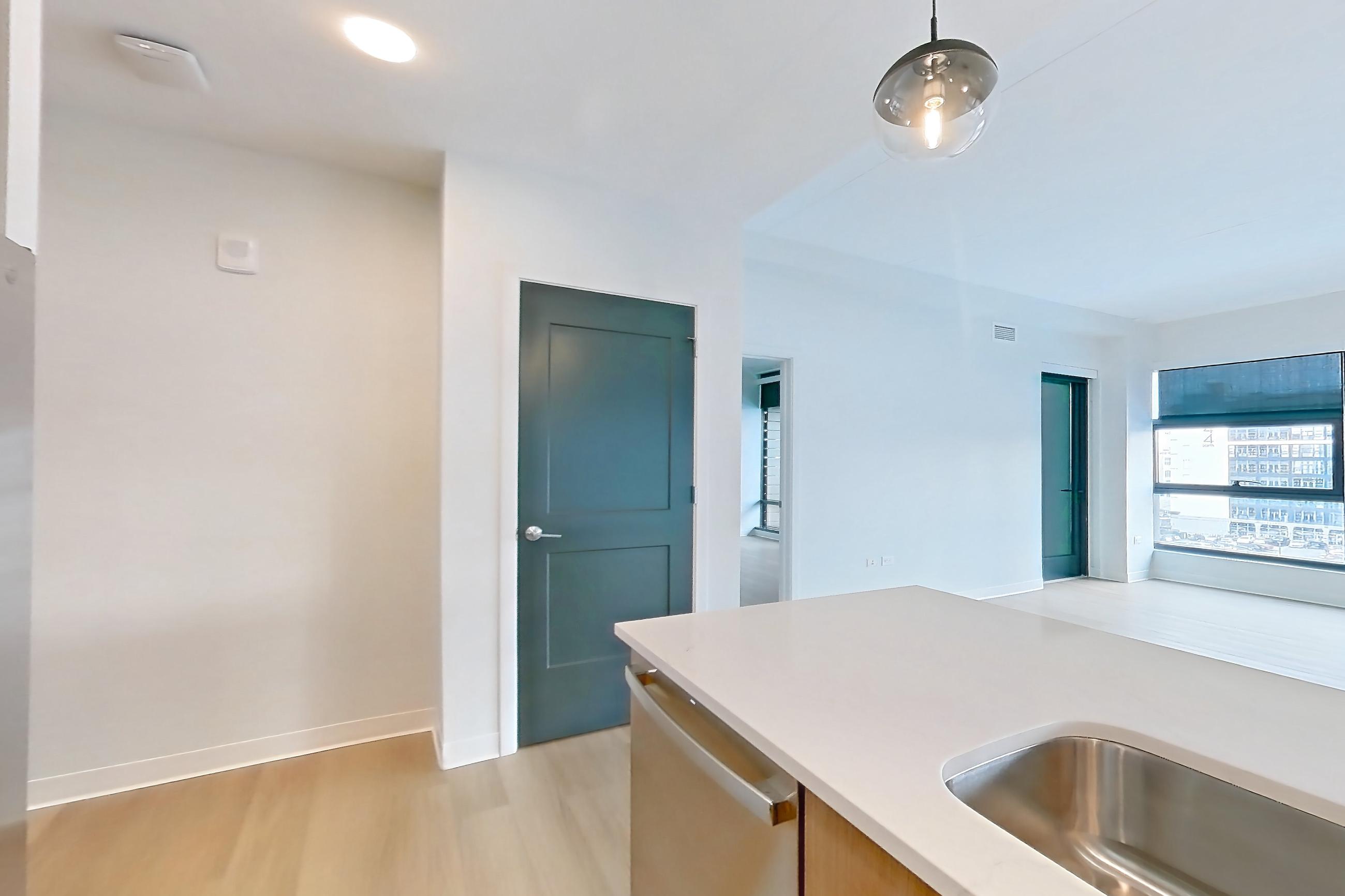 Kitchen with dishwasher, electric range, kitchen island, light countertops, light stone countertops, light wood-finish flooring, oven/range, refrigerator, stainless steel appliances, and water & ice dispenser, Apartment 0536 at The Alcott