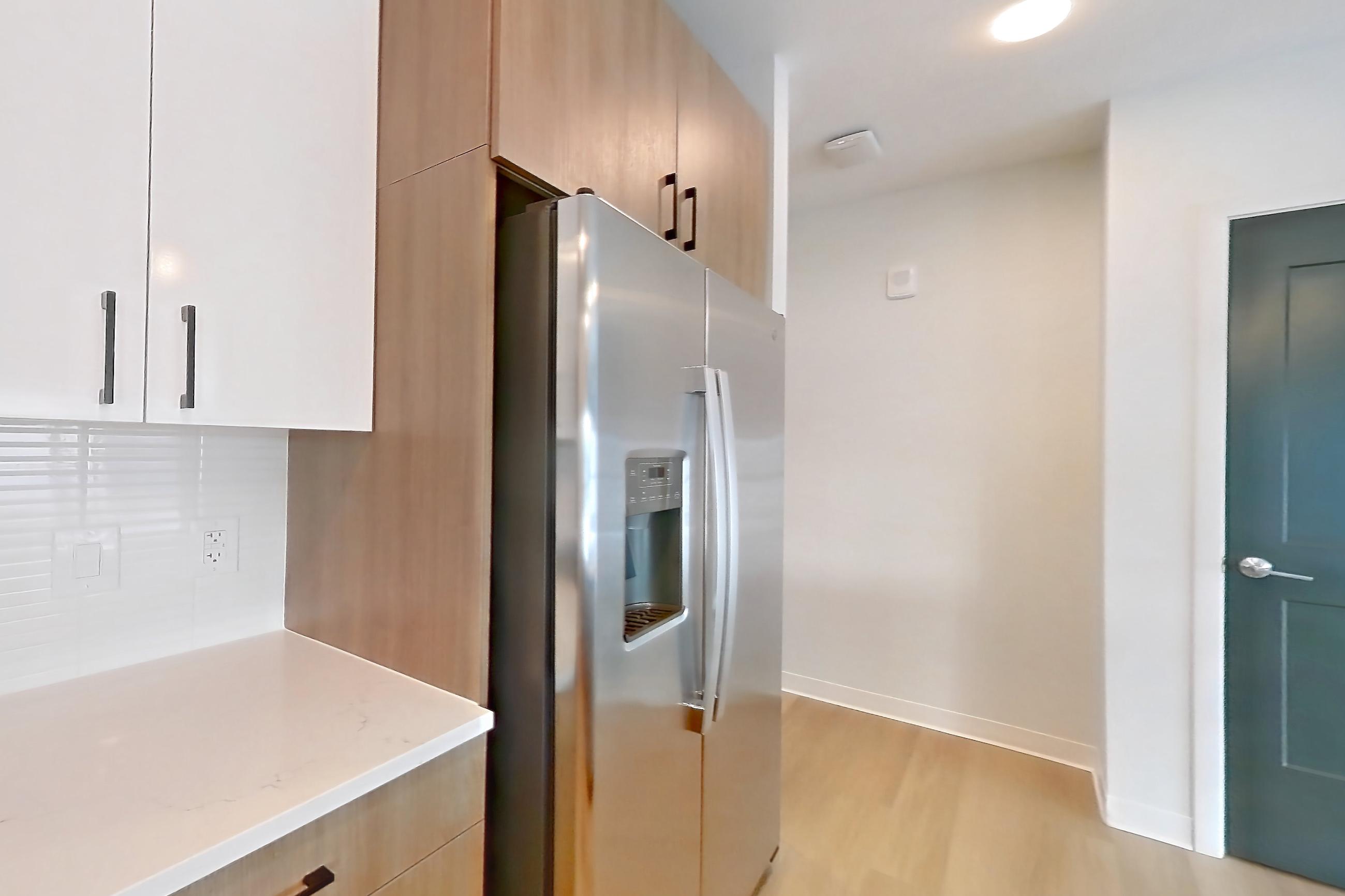 Kitchen with dishwasher, electric range, kitchen island, light countertops, light stone countertops, light wood-finish flooring, oven/range, refrigerator, stainless steel appliances, and water & ice dispenser, Apartment 0536 at The Alcott
