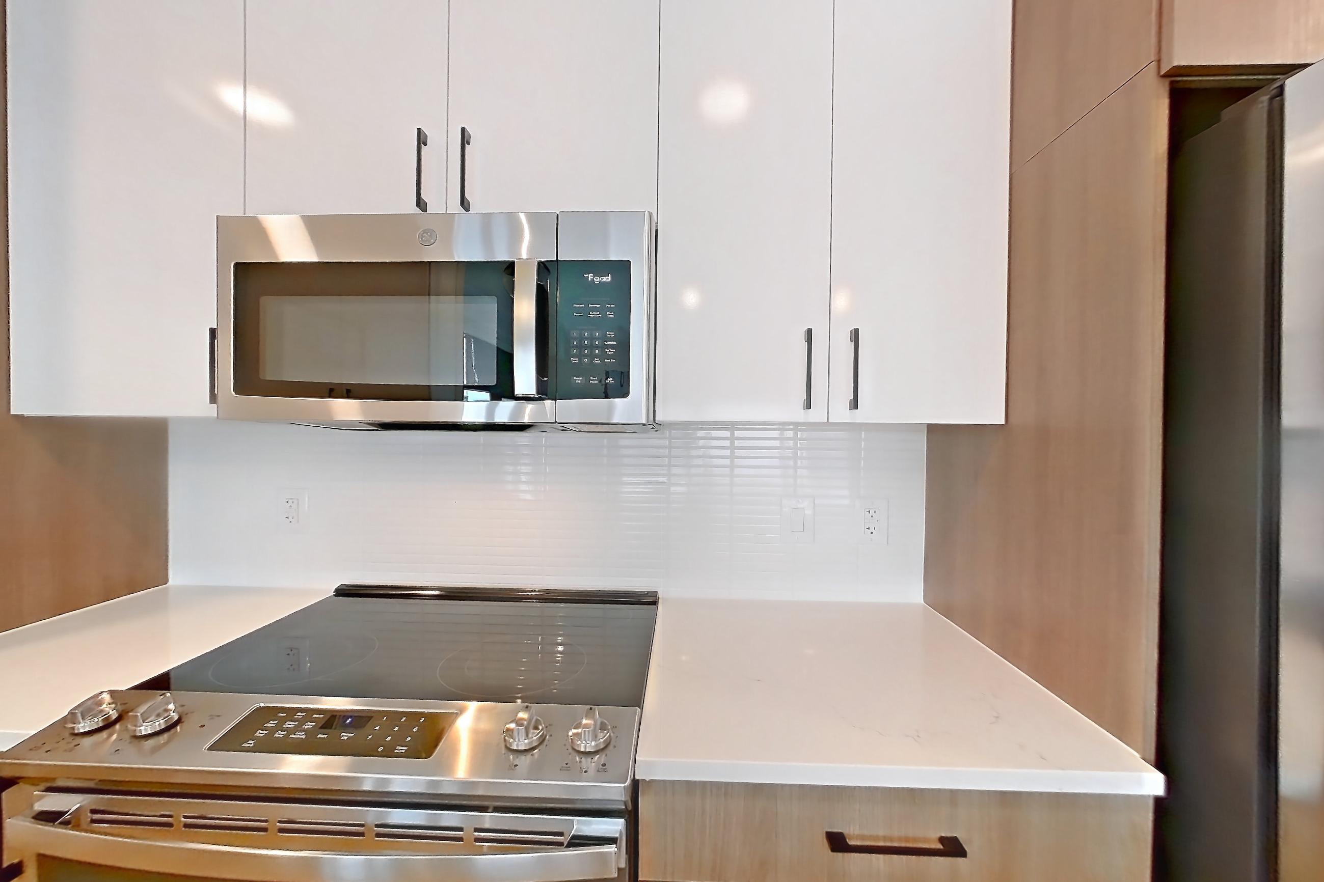Kitchen with dishwasher, electric range, kitchen island, light countertops, light stone countertops, light wood-finish flooring, oven/range, refrigerator, stainless steel appliances, and water & ice dispenser, Apartment 0536 at The Alcott