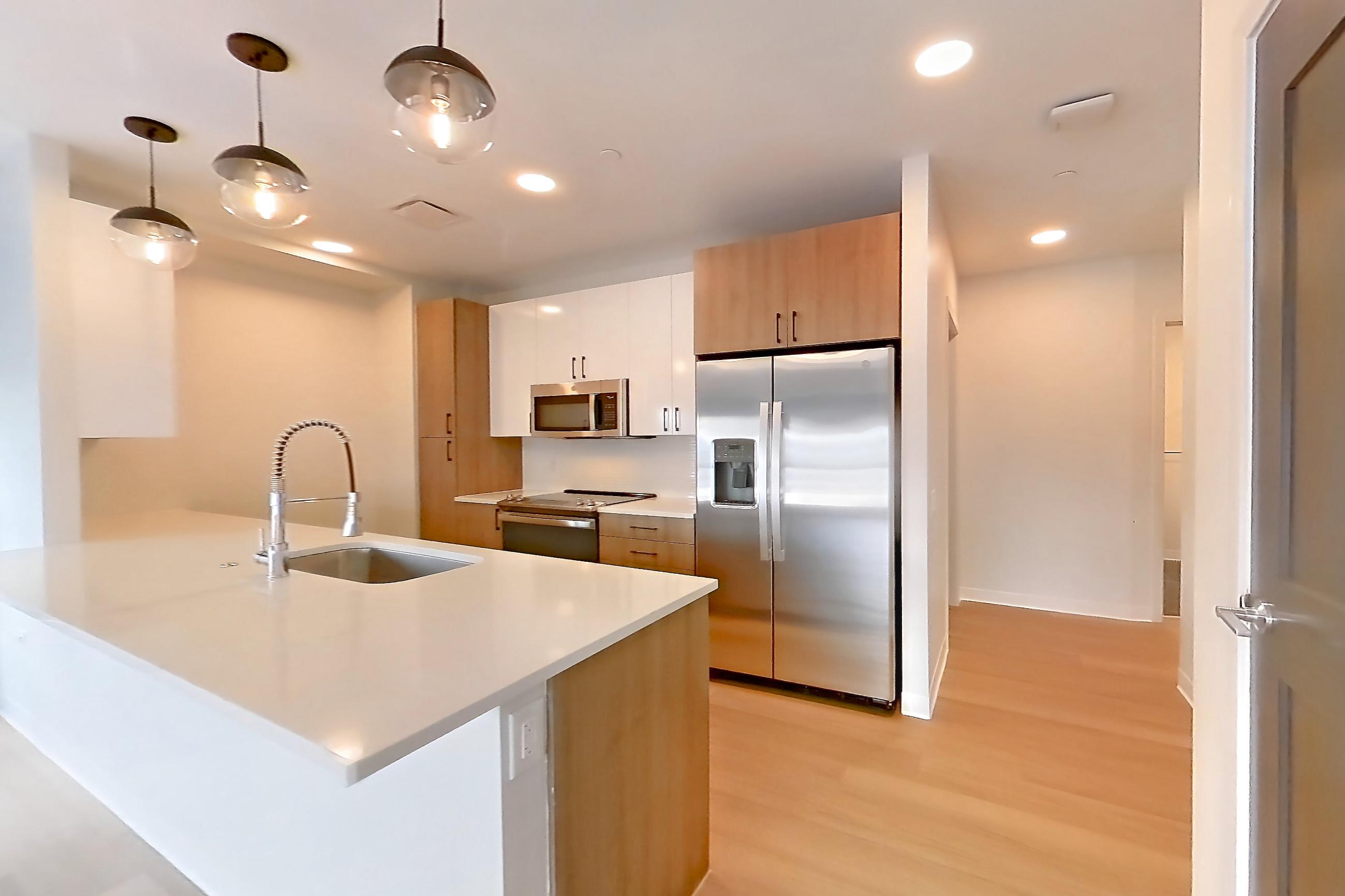 Living space with electric range, light countertops, light wood-finish flooring, microwave, oven/range, refrigerator, and stainless steel appliances, Apartment 0536 at The Alcott