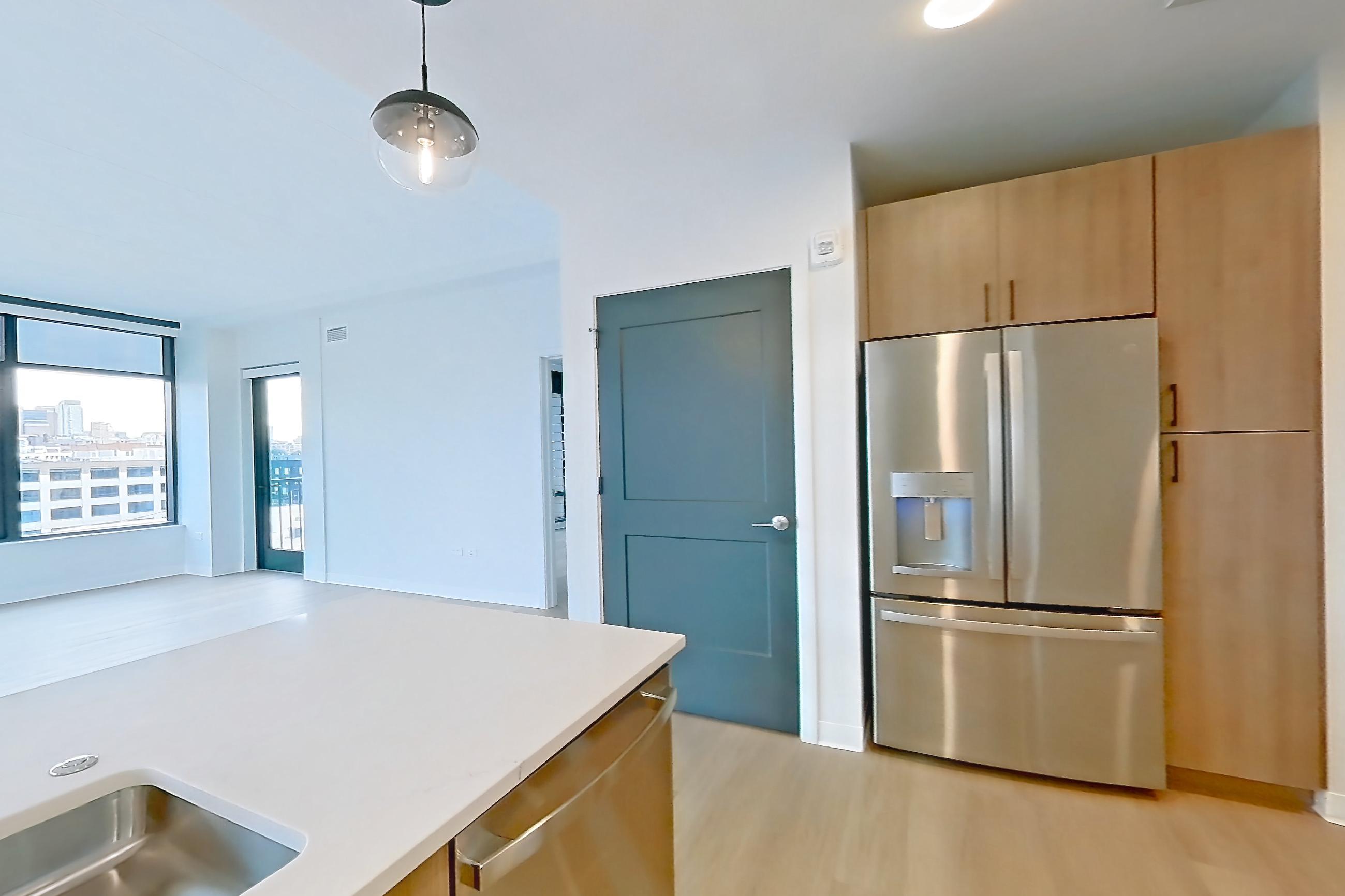Kitchen with dishwasher, light countertops, light stone countertops, light wood-finish flooring, microwave, oven/range, refrigerator, stainless steel appliances, and water & ice dispenser, Apartment 0537 at The Alcott