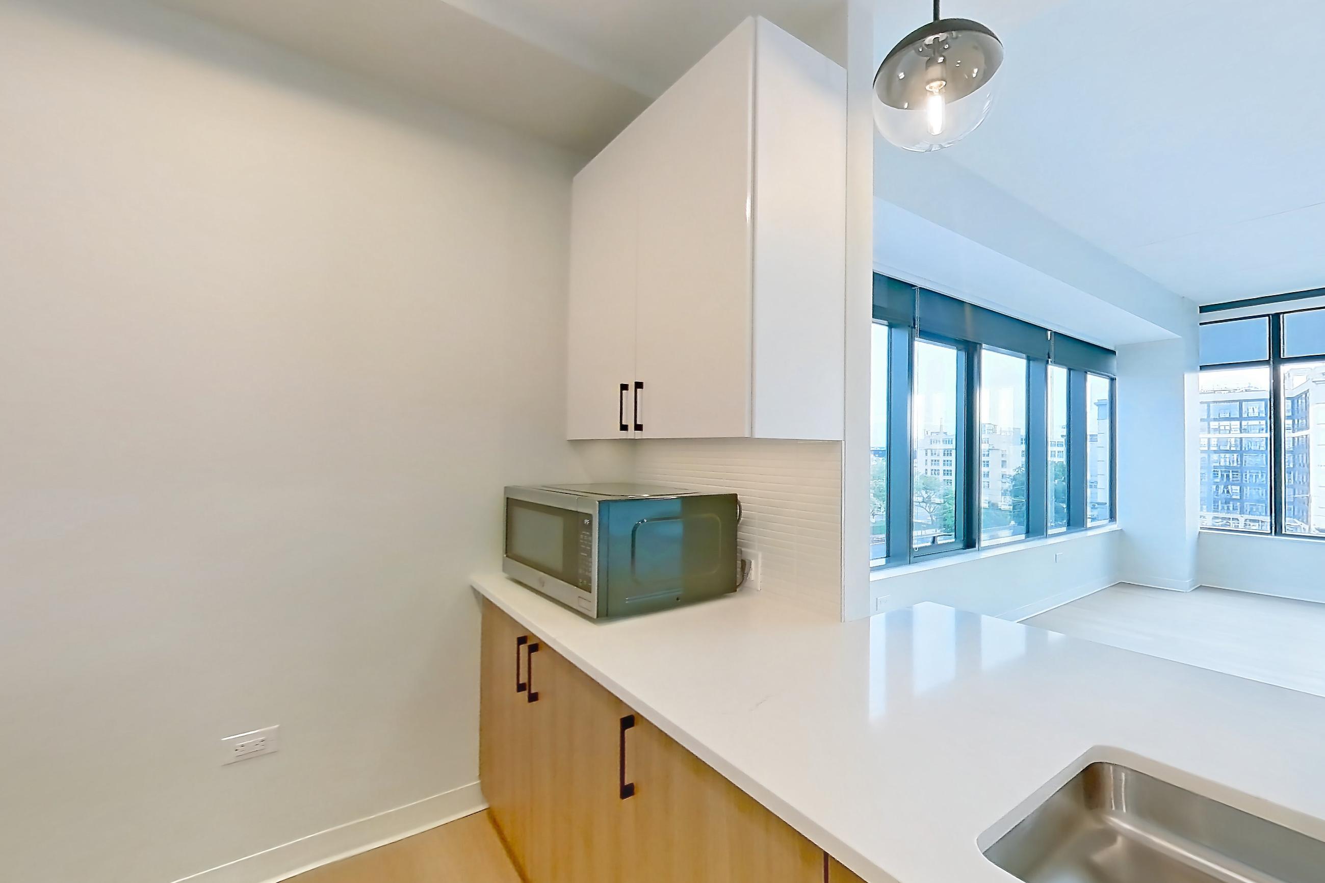 Kitchen with dishwasher, light countertops, light stone countertops, light wood-finish flooring, microwave, oven/range, refrigerator, stainless steel appliances, and water & ice dispenser, Apartment 0537 at The Alcott