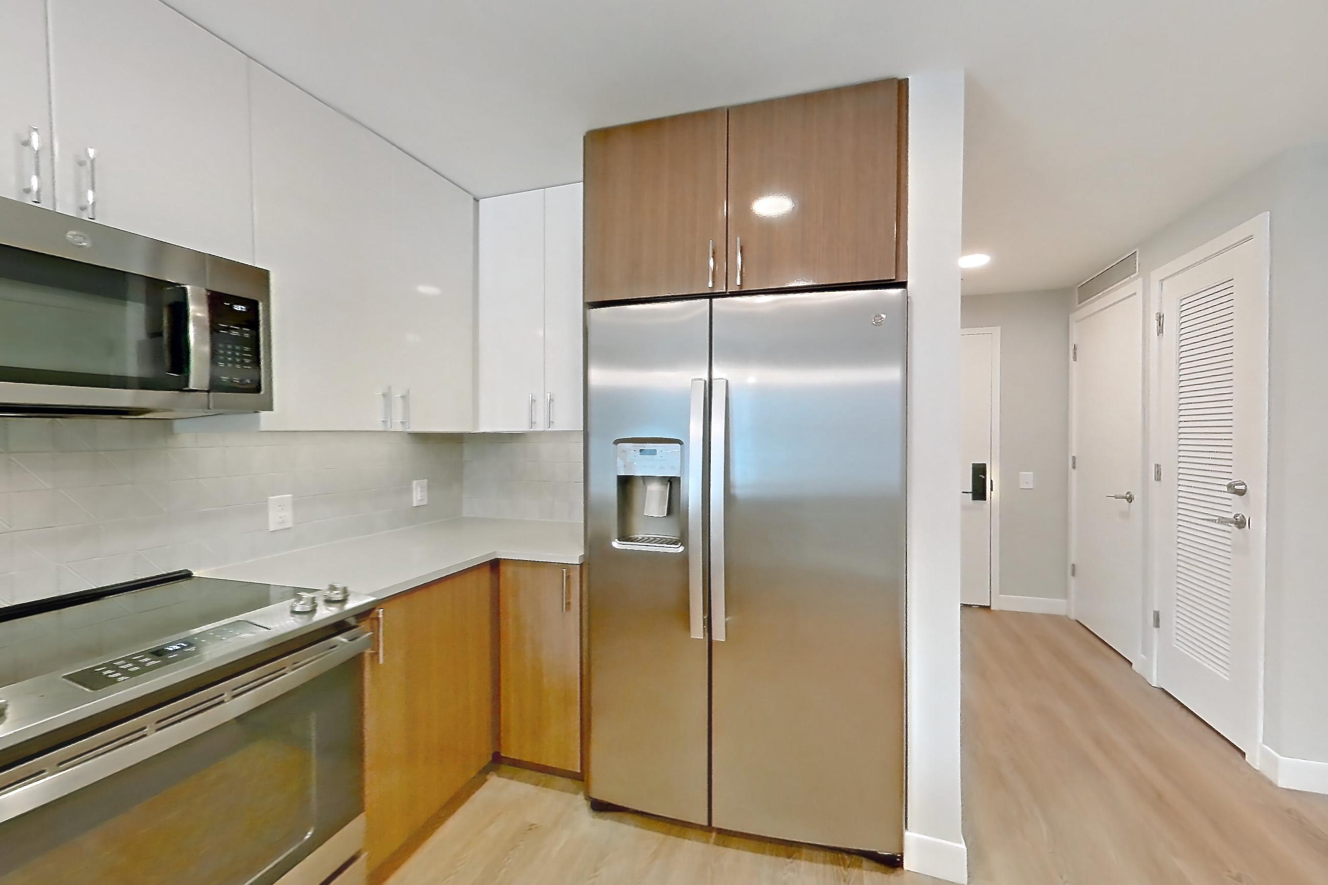Kitchen with dishwasher, electric range, light countertops, light stone countertops, light wood-finish flooring, microwave, oven/range, refrigerator, stainless steel appliances, and water & ice dispenser, Apartment 0802 at Josephine