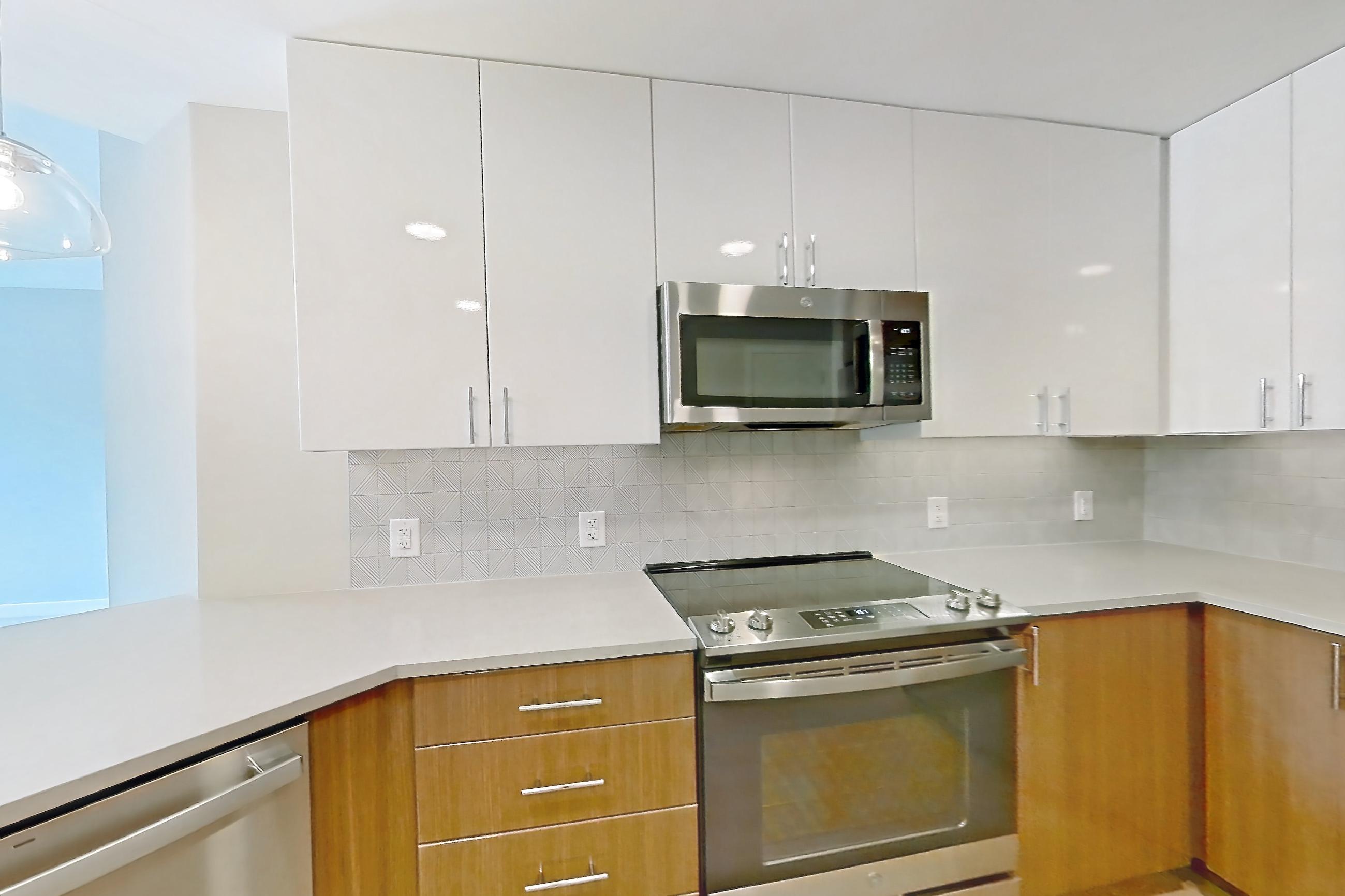Kitchen with dishwasher, electric range, light countertops, light stone countertops, light wood-finish flooring, microwave, oven/range, refrigerator, stainless steel appliances, and water & ice dispenser, Apartment 0802 at Josephine