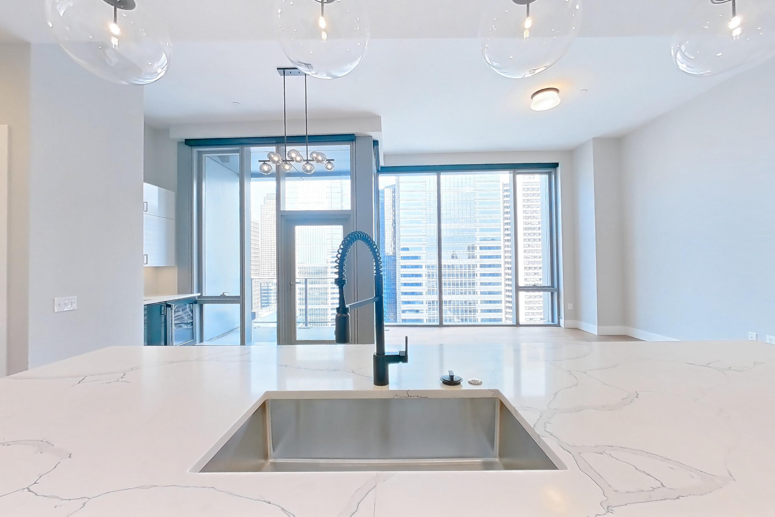 Kitchen with dishwasher, double oven, kitchen island, light countertops, light stone countertops, light wood-finish flooring, refrigerator, and stainless steel appliances, Apartment 2603 at Josephine