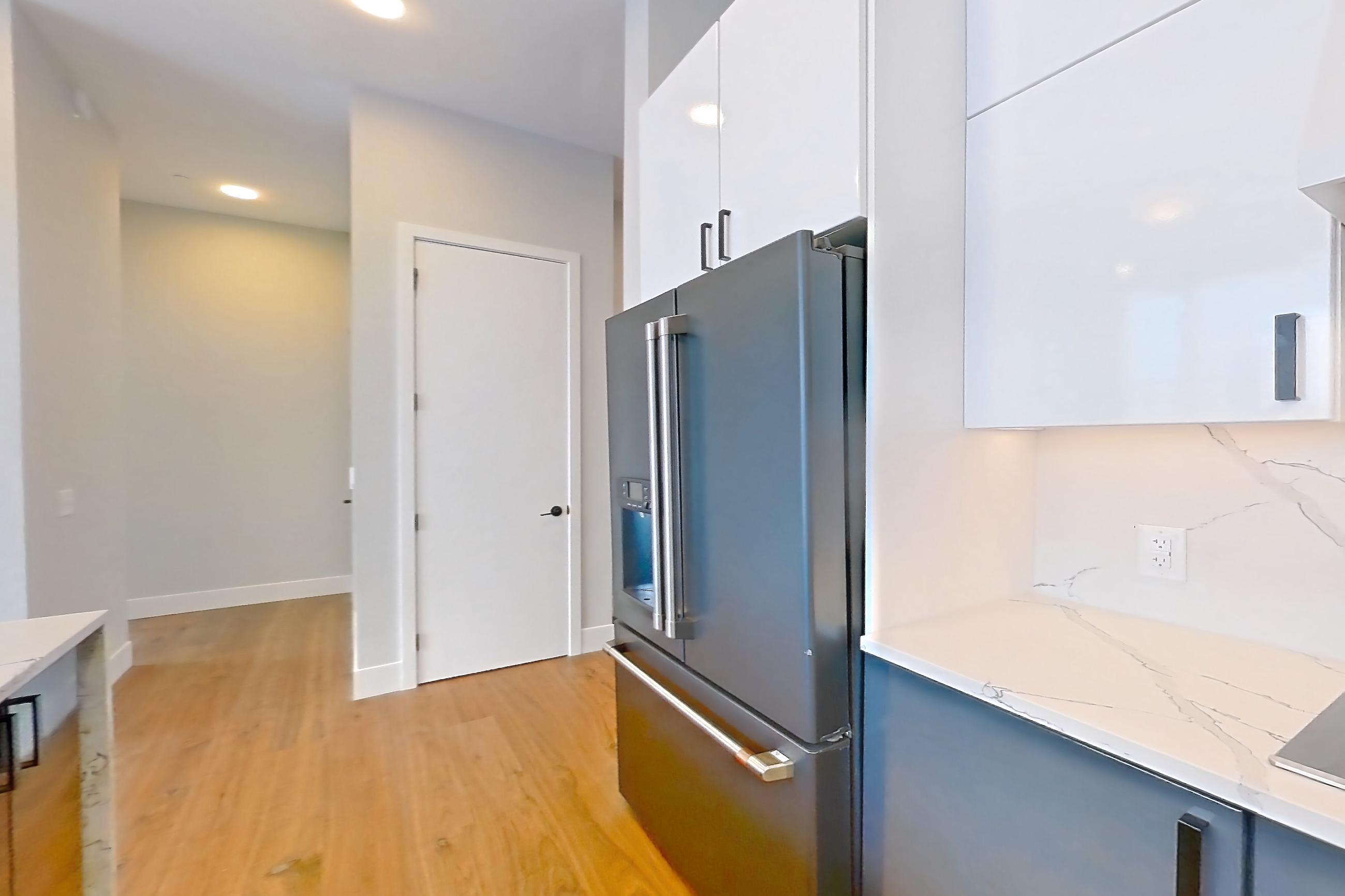 Kitchen with dishwasher, double oven, kitchen island, light countertops, light stone countertops, light wood-finish flooring, refrigerator, and stainless steel appliances, Apartment 2603 at Josephine