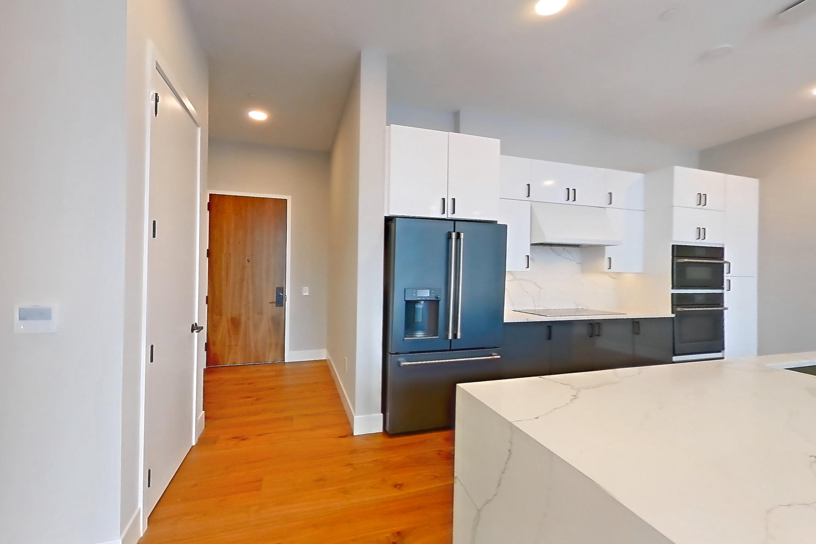 Living space with black appliances, cooktop, electric cooktop, kitchen island, light countertops, light stone countertops, light wood-finish flooring, oven/range, range hood, refrigerator, and water & ice dispenser, Apartment 2603 at Josephine