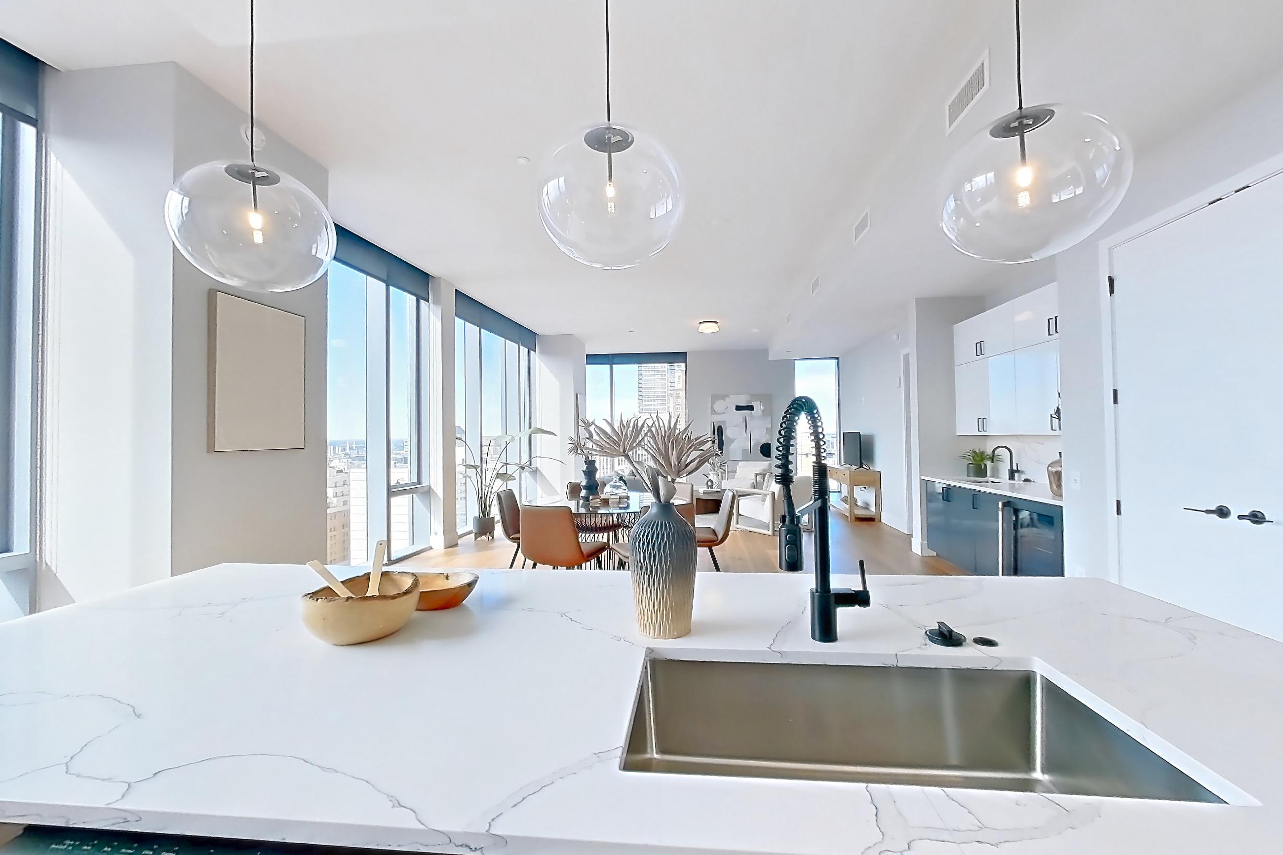 Kitchen with dishwasher, double oven, kitchen island, light countertops, light stone countertops, light wood-finish flooring, refrigerator, stainless steel appliances, and water & ice dispenser, Apartment 2601 at Josephine