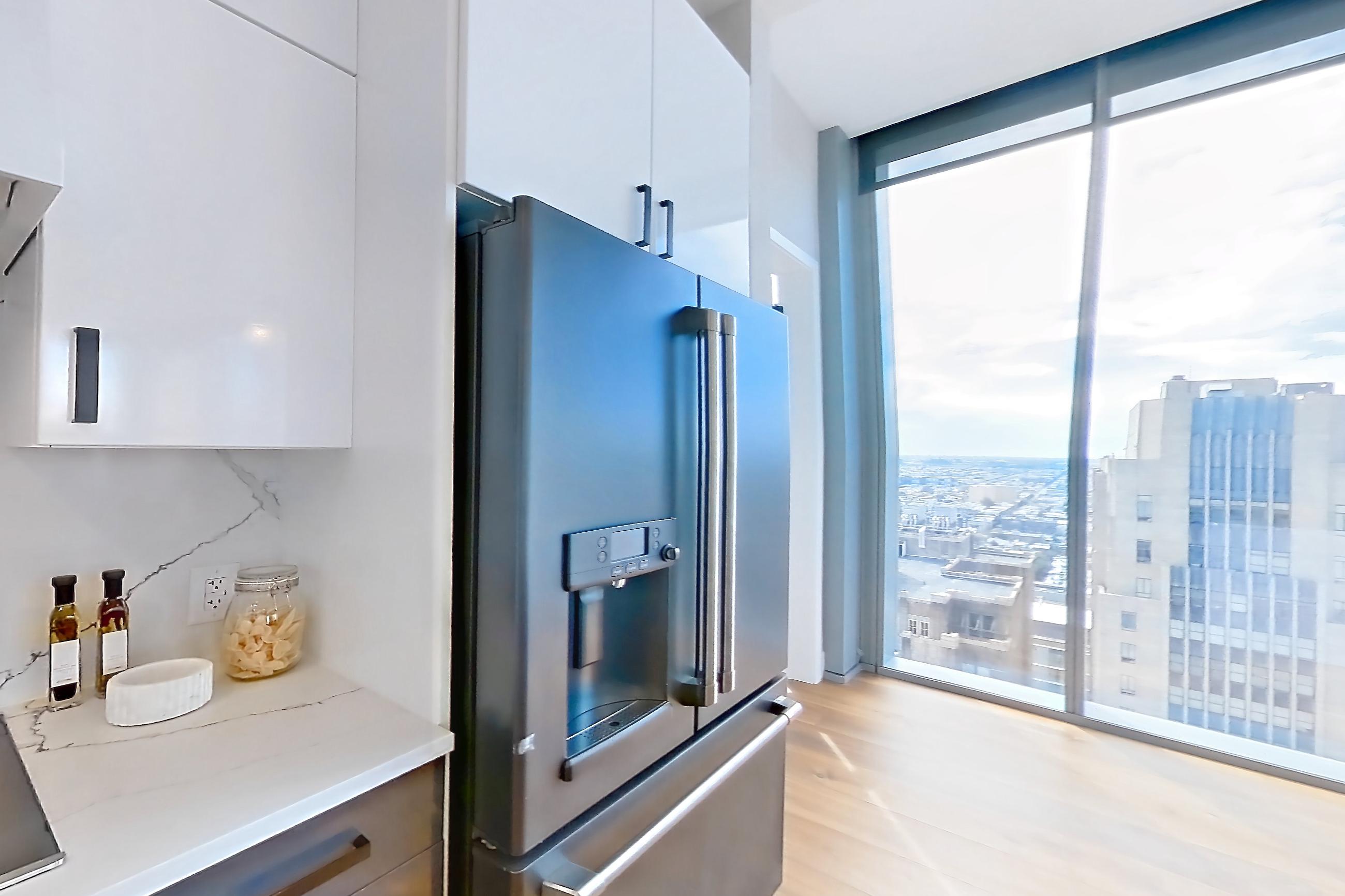 Kitchen with dishwasher, double oven, kitchen island, light countertops, light stone countertops, light wood-finish flooring, refrigerator, stainless steel appliances, and water & ice dispenser, Apartment 2601 at Josephine
