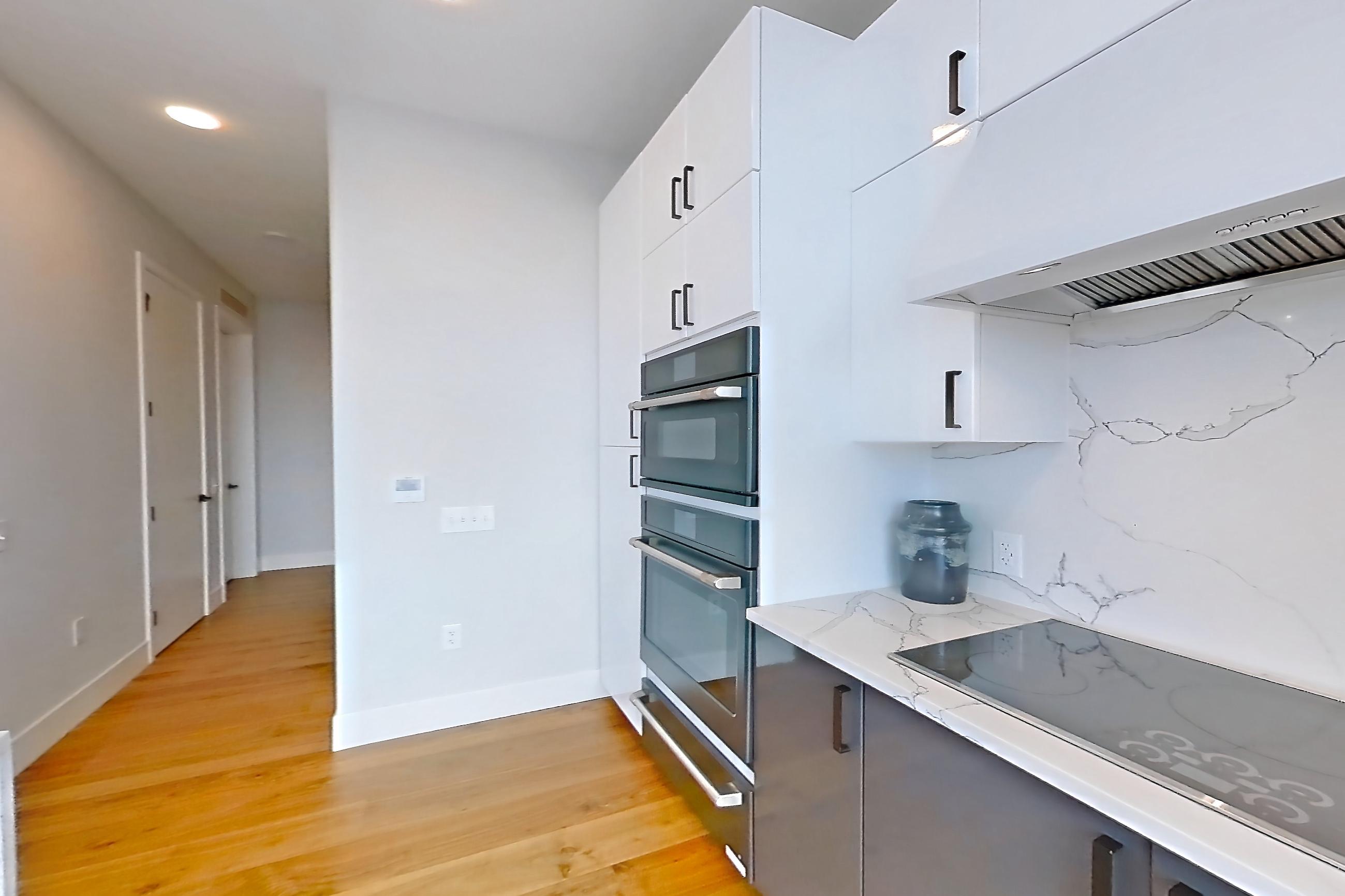 Kitchen with dishwasher, double oven, kitchen island, light countertops, light stone countertops, light wood-finish flooring, refrigerator, stainless steel appliances, and water & ice dispenser, Apartment 2601 at Josephine