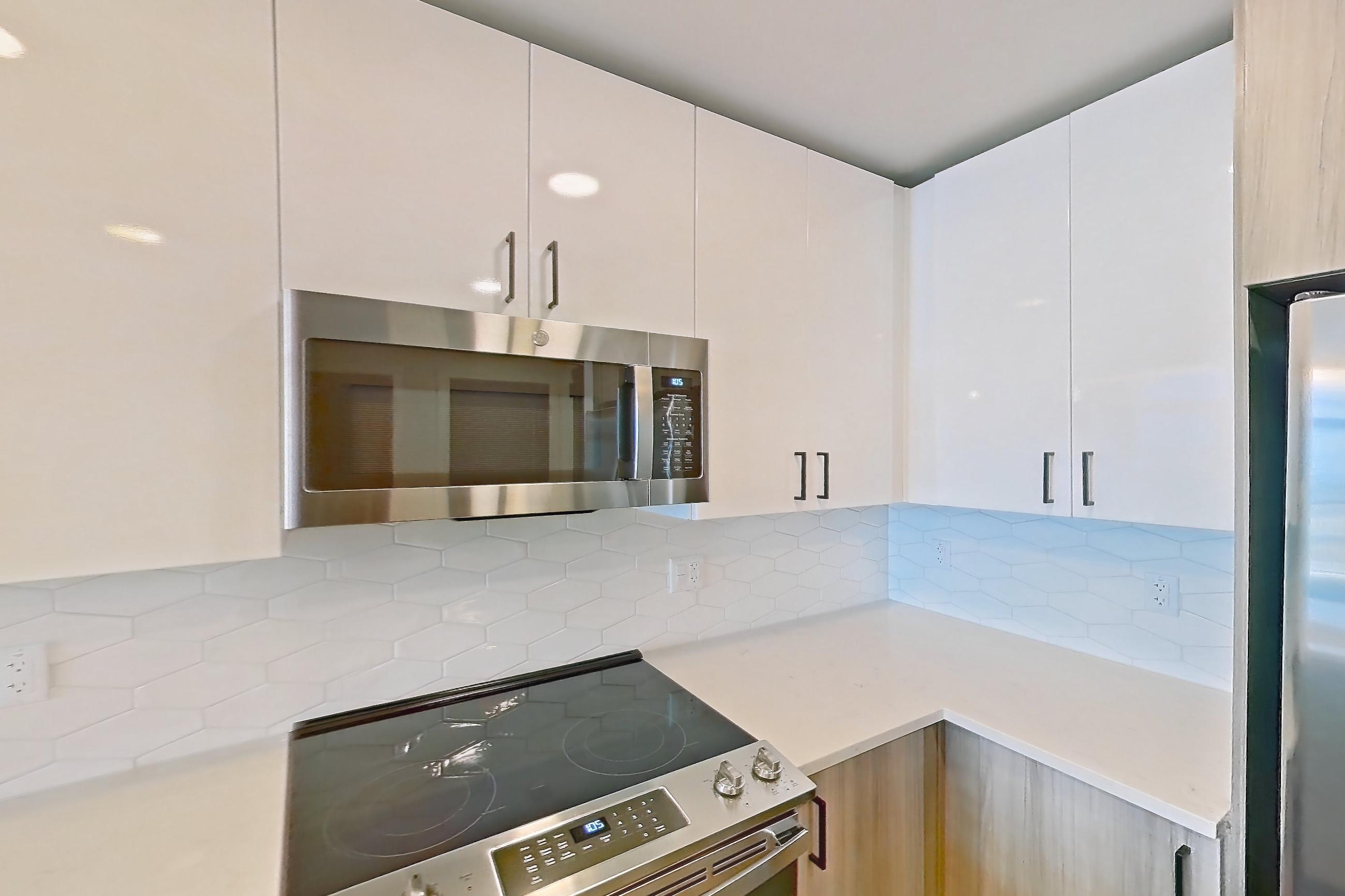 Kitchen with dishwasher, electric range, light countertops, light stone countertops, light wood-finish flooring, microwave, oven/range, range hood, and stainless steel appliances, Apartment 1917 at Deco 969