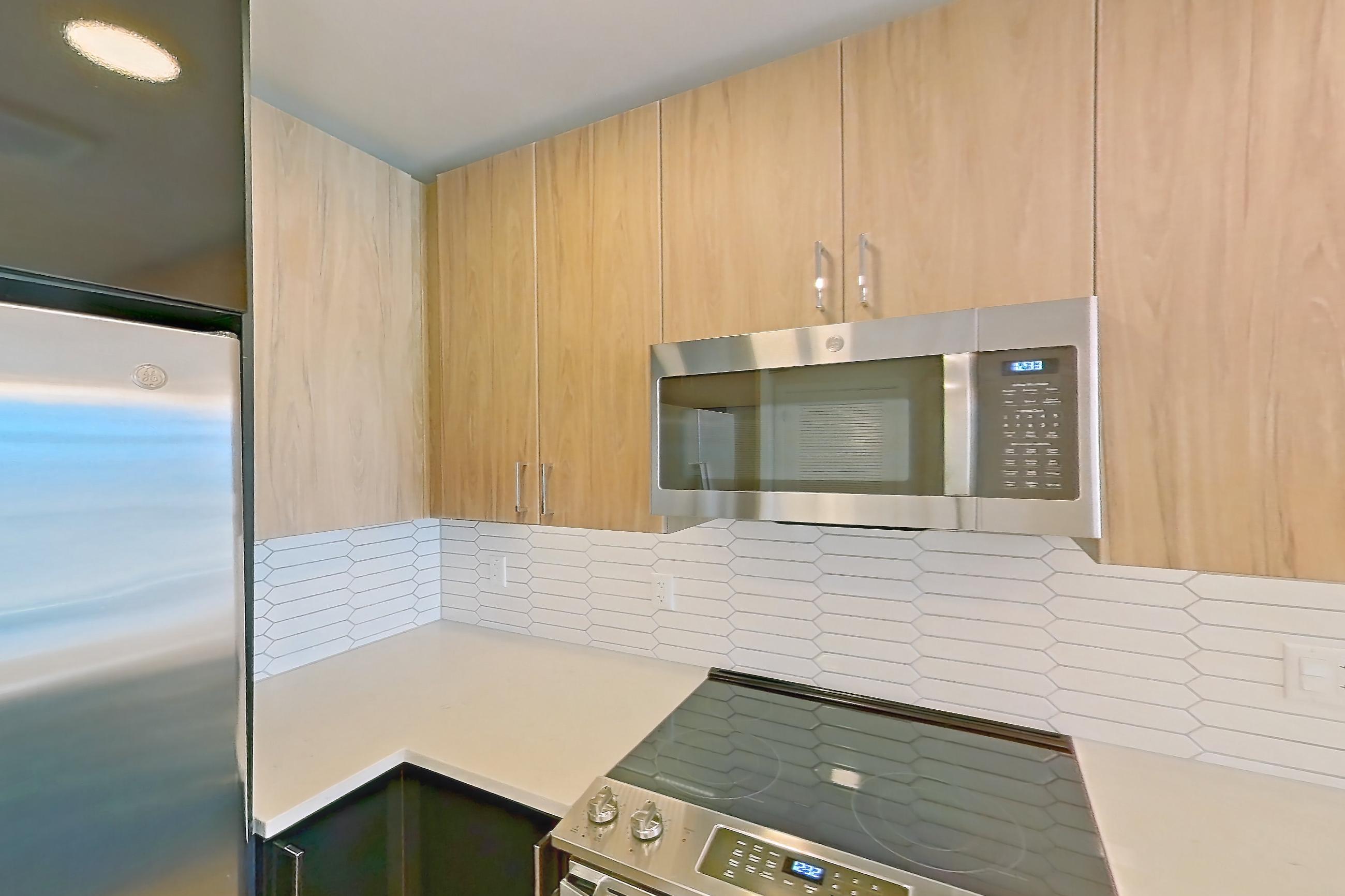 Kitchen with electric range, light countertops, light stone countertops, light wood-finish flooring, microwave, oven/range, refrigerator, stainless steel appliances, and water & ice dispenser, Apartment 1822 at Deco 969