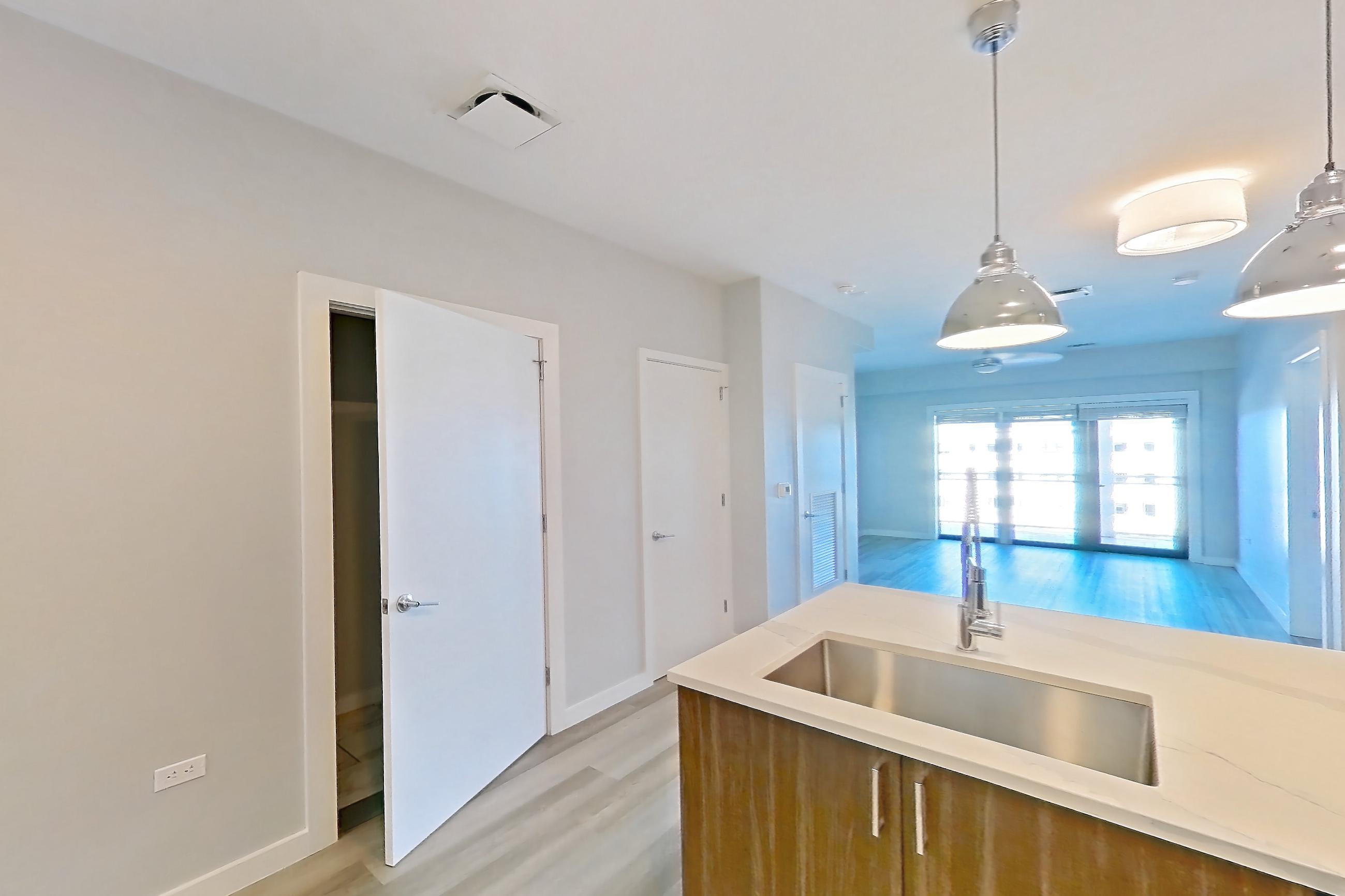 Kitchen with dishwasher, gas range, kitchen island, light countertops, light stone countertops, light wood-finish flooring, microwave, oven/range, refrigerator, stainless steel appliances, and water & ice dispenser, Apartment S402 at Carlow Wind Watch