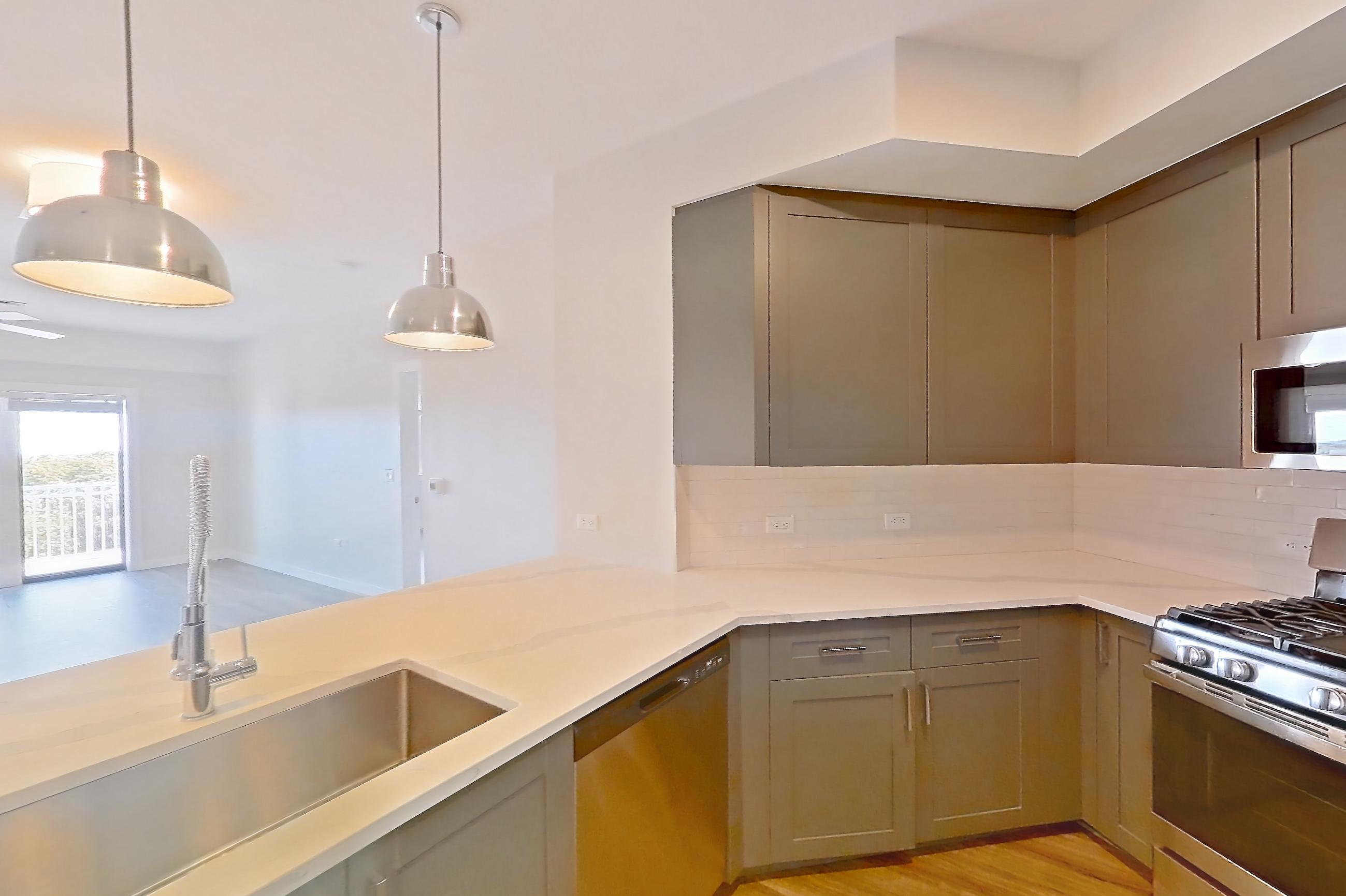 Kitchen with dishwasher, gas range, light countertops, light stone countertops, light wood-finish flooring, microwave, oven/range, refrigerator, stainless steel appliances, and water & ice dispenser, Apartment S506 at Carlow Wind Watch