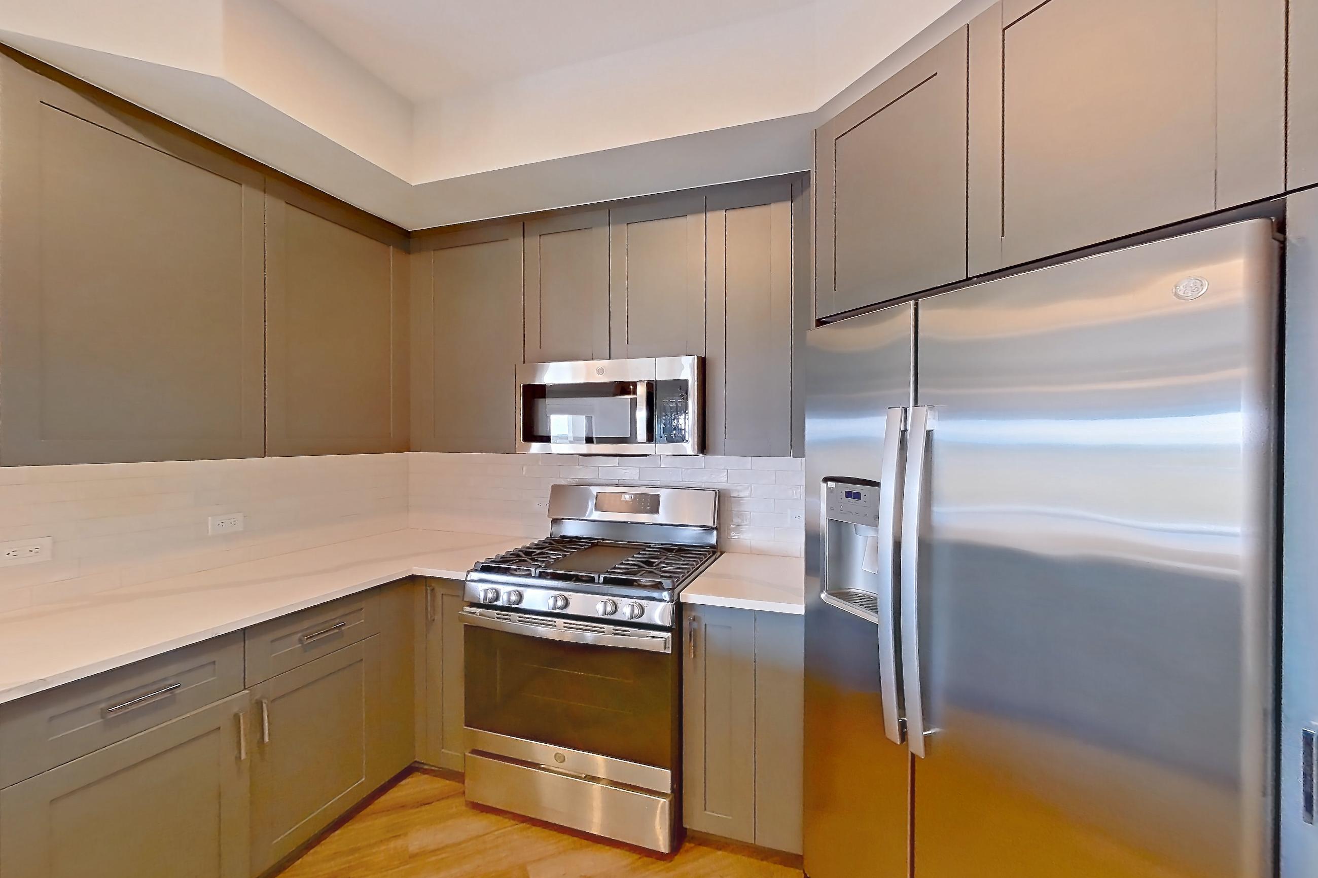 Kitchen with dishwasher, gas range, light countertops, light stone countertops, light wood-finish flooring, microwave, oven/range, refrigerator, stainless steel appliances, and water & ice dispenser, Apartment S506 at Carlow Wind Watch