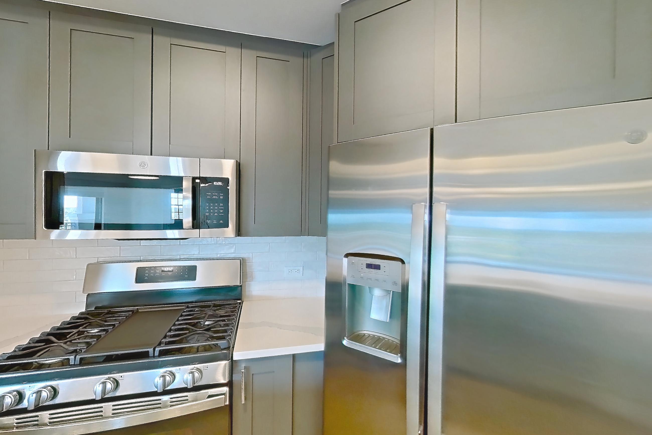 Kitchen with dishwasher, gas range, light countertops, light stone countertops, light wood-finish flooring, microwave, oven/range, refrigerator, stainless steel appliances, and water & ice dispenser, Apartment S306 at Carlow Wind Watch