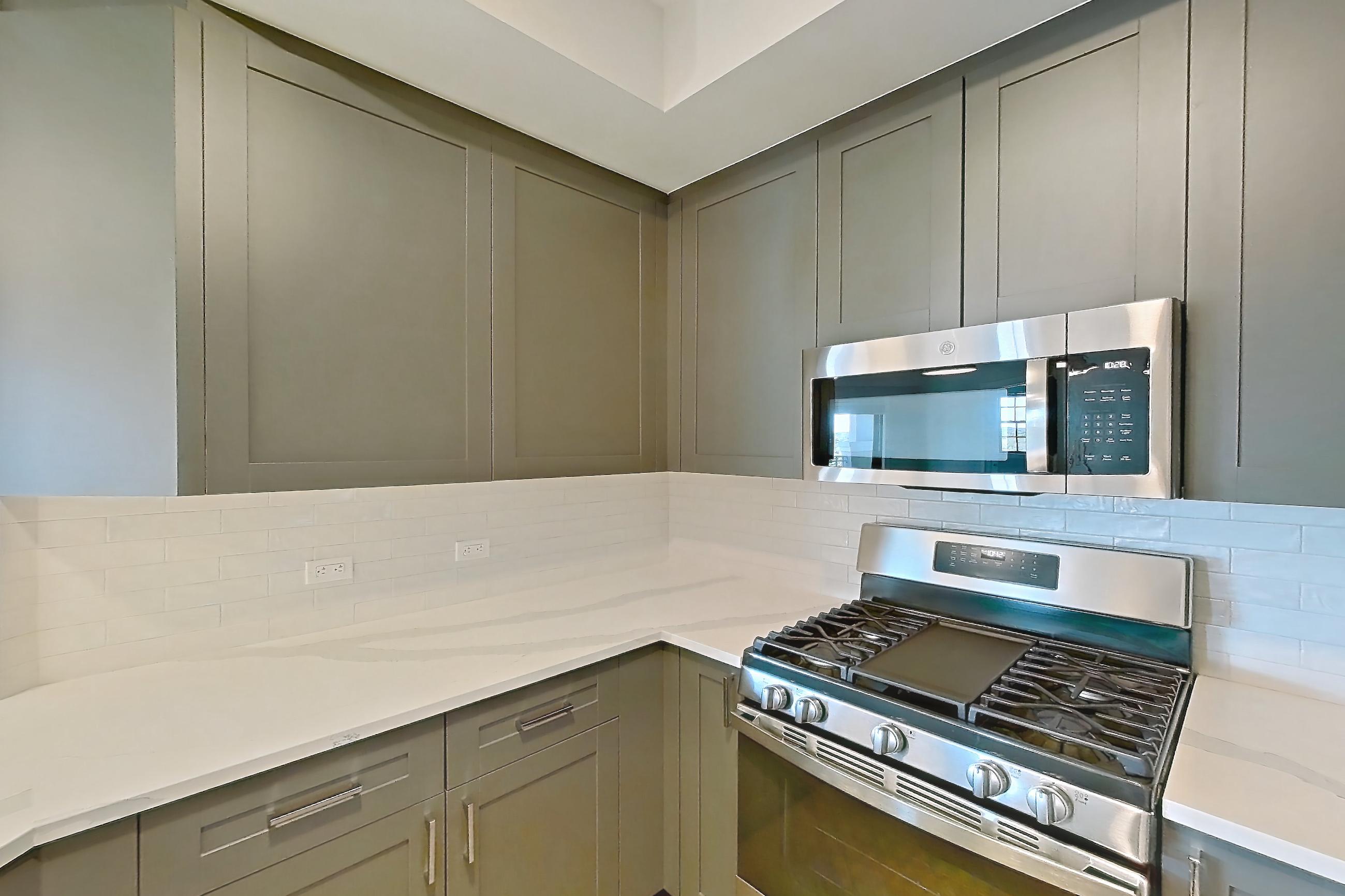 Kitchen with dishwasher, gas range, light countertops, light stone countertops, light wood-finish flooring, microwave, oven/range, refrigerator, stainless steel appliances, and water & ice dispenser, Apartment S306 at Carlow Wind Watch