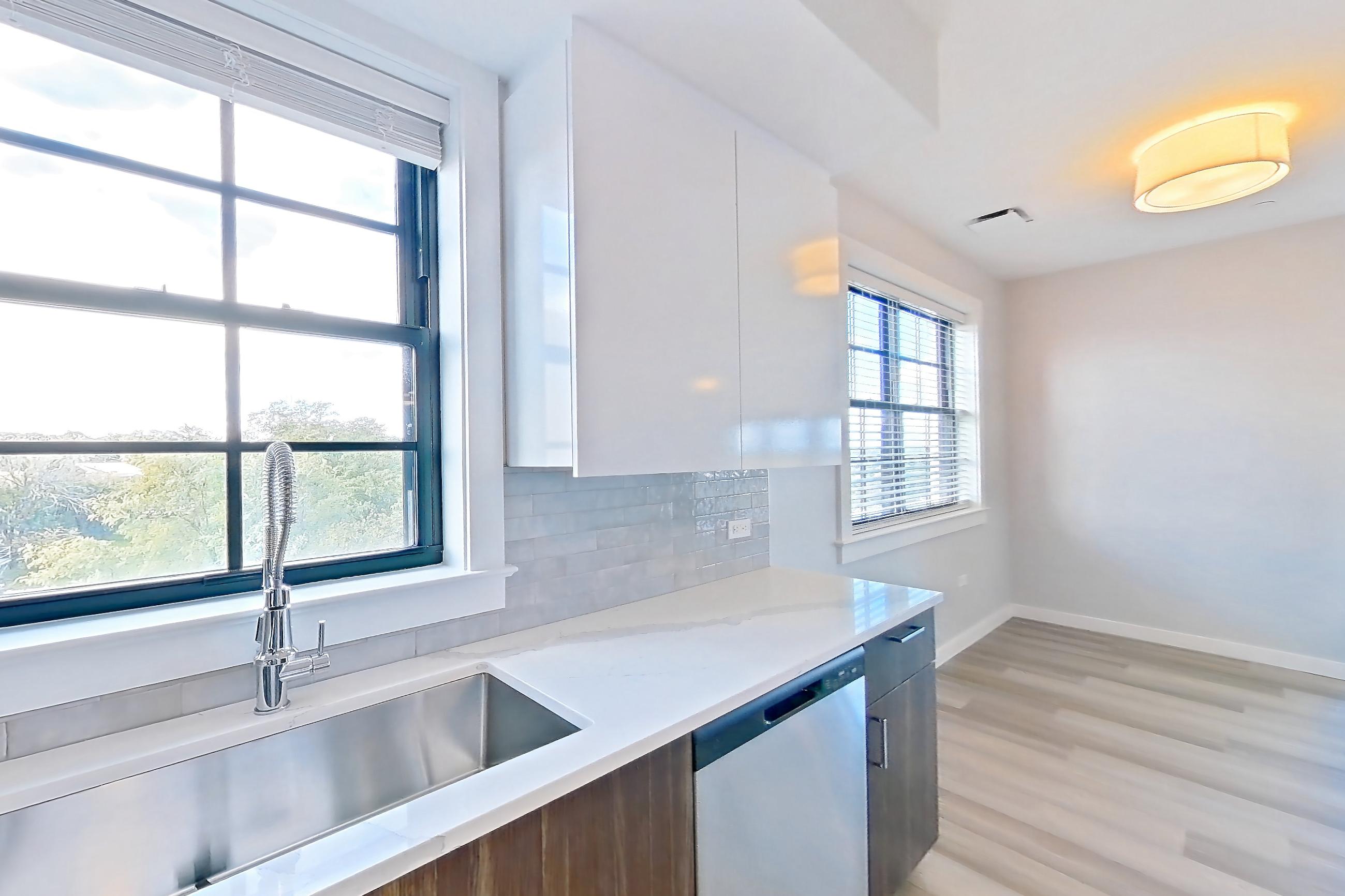 Kitchen with dishwasher, gas range, light countertops, light stone countertops, light wood-finish flooring, microwave, oven/range, refrigerator, stainless steel appliances, and water & ice dispenser, Apartment N416 at Carlow Wind Watch