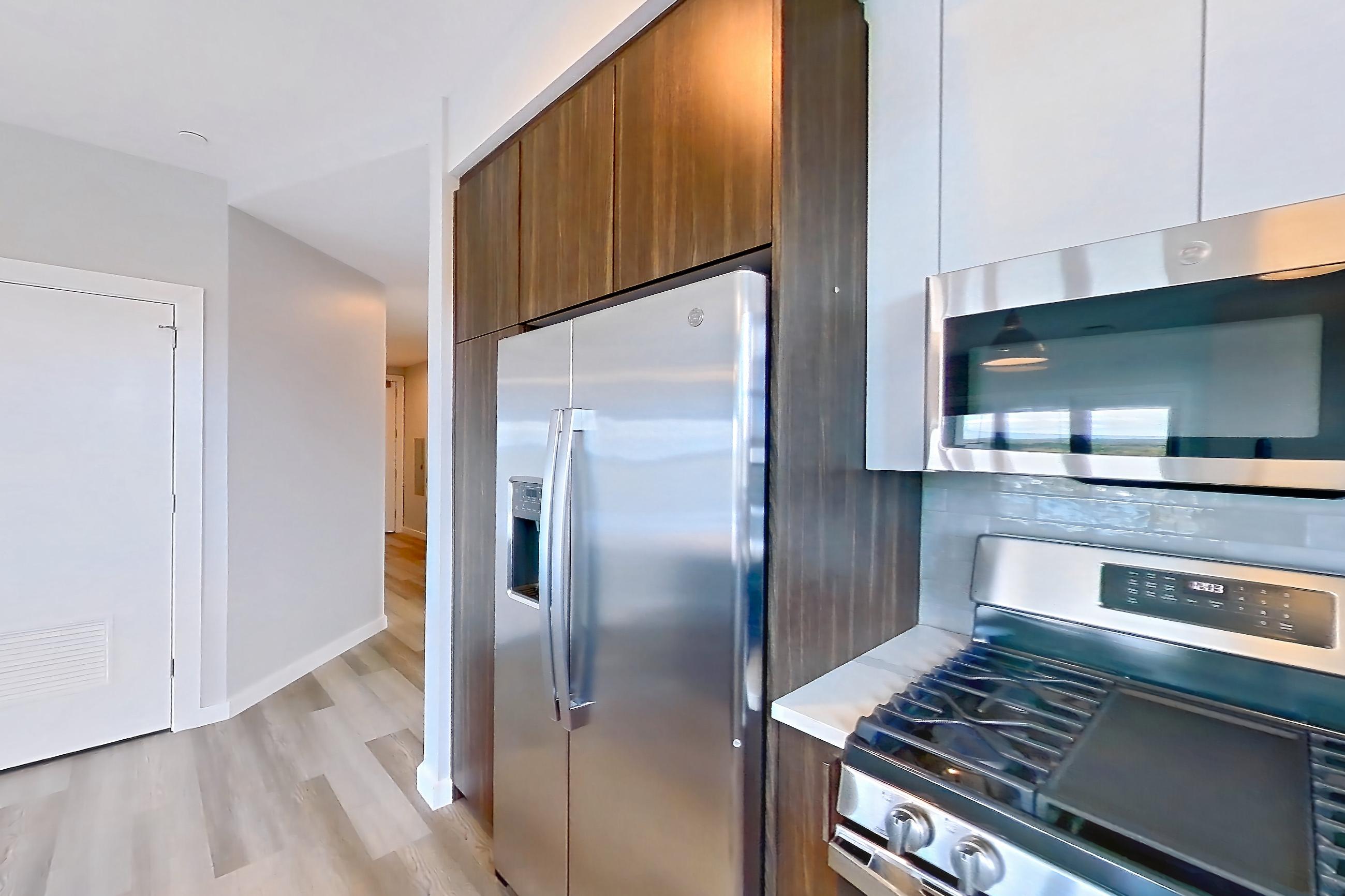 Kitchen with dishwasher, gas range, light countertops, light stone countertops, light wood-finish flooring, microwave, oven/range, refrigerator, stainless steel appliances, and water & ice dispenser, Apartment N416 at Carlow Wind Watch