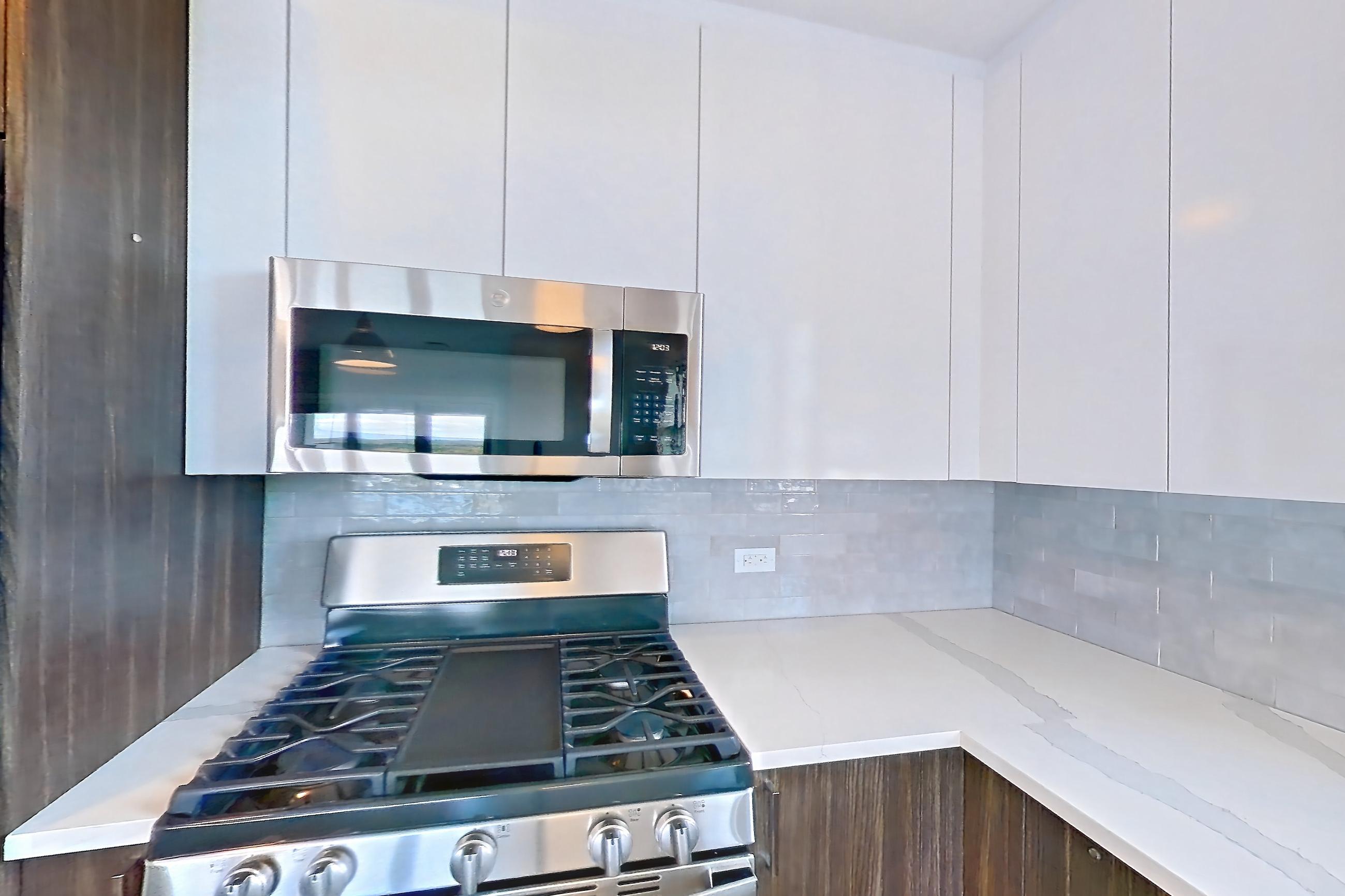 Kitchen with dishwasher, gas range, light countertops, light stone countertops, light wood-finish flooring, microwave, oven/range, refrigerator, stainless steel appliances, and water & ice dispenser, Apartment N416 at Carlow Wind Watch