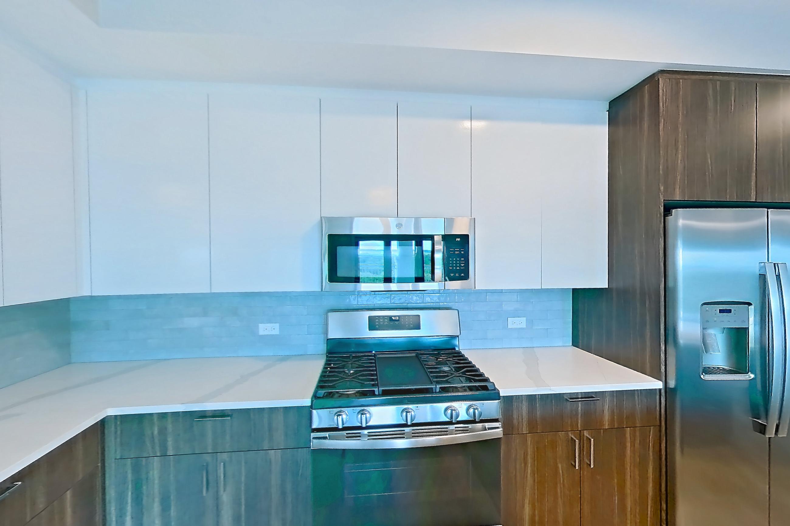 Kitchen with gas range, light stone countertops, light wood-finish flooring, microwave, oven/range, refrigerator, stainless steel appliances, and water & ice dispenser, Apartment N201 at Carlow Wind Watch
