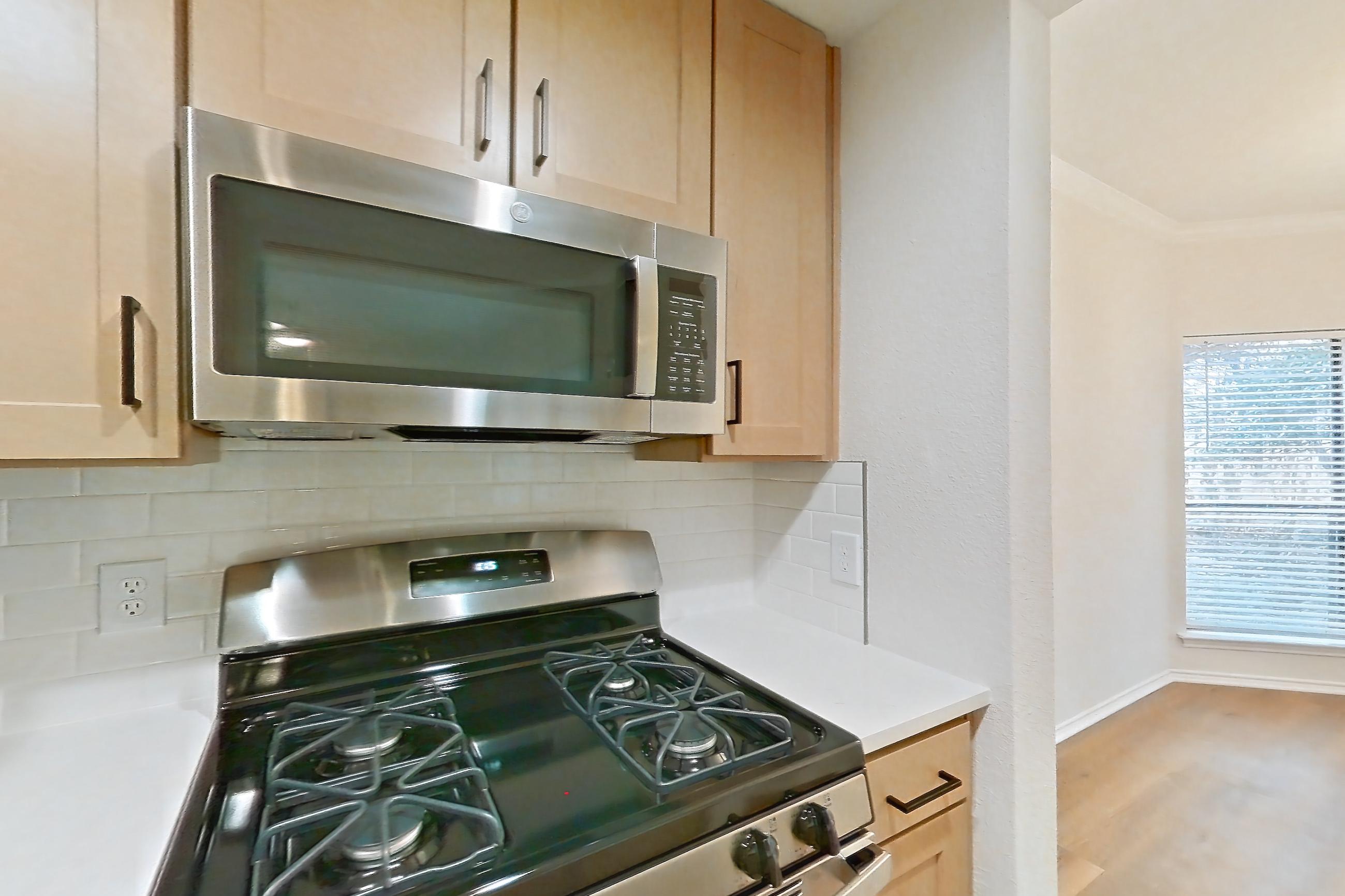 Kitchen with dishwasher, gas range, light countertops, light stone countertops, light wood-finish flooring, microwave, oven/range, refrigerator, and stainless steel appliances, Apartment 1805 at Marquis at Caprock Canyon