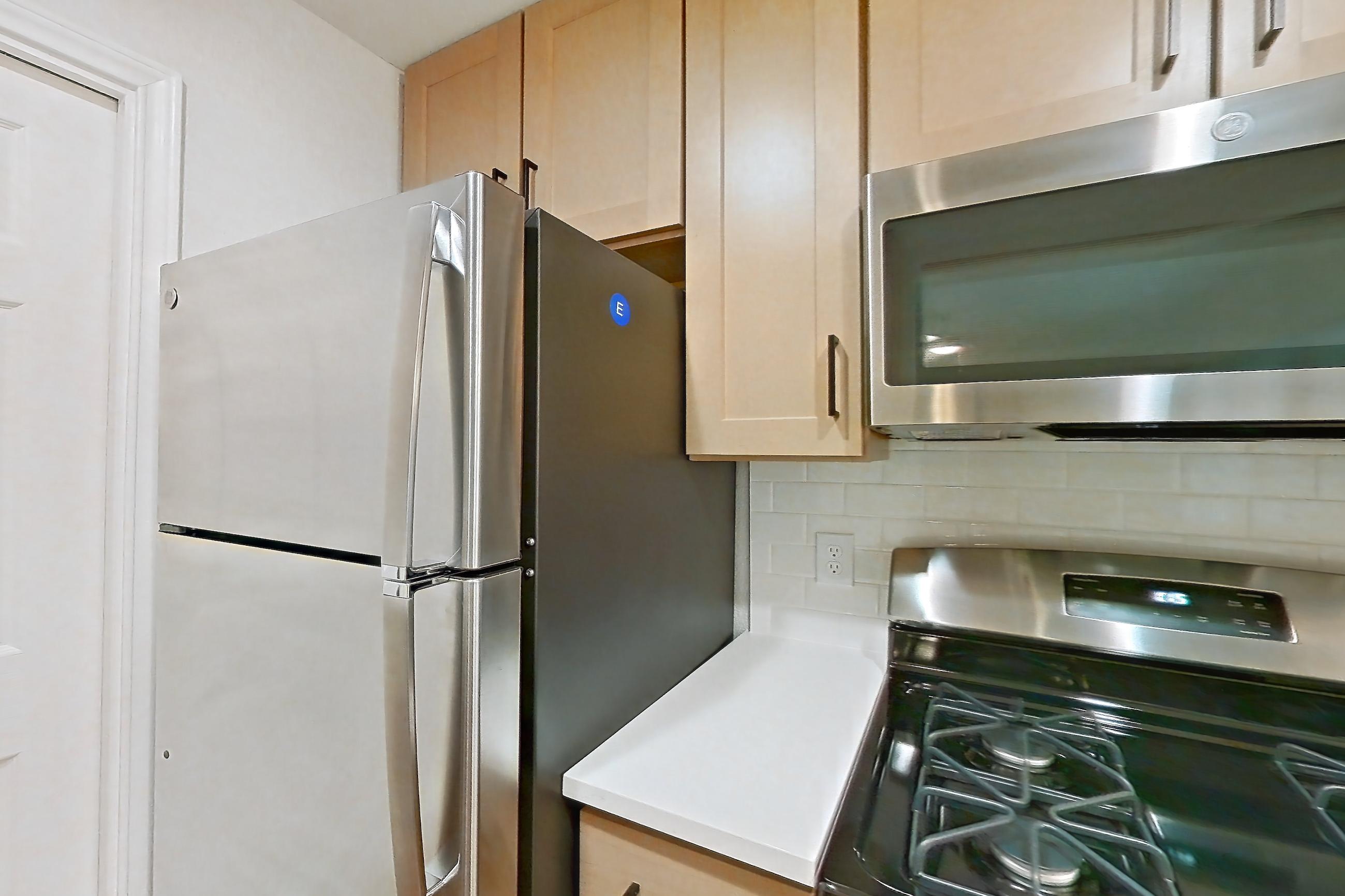 Kitchen with dishwasher, gas range, light countertops, light stone countertops, light wood-finish flooring, microwave, oven/range, refrigerator, and stainless steel appliances, Apartment 1805 at Marquis at Caprock Canyon