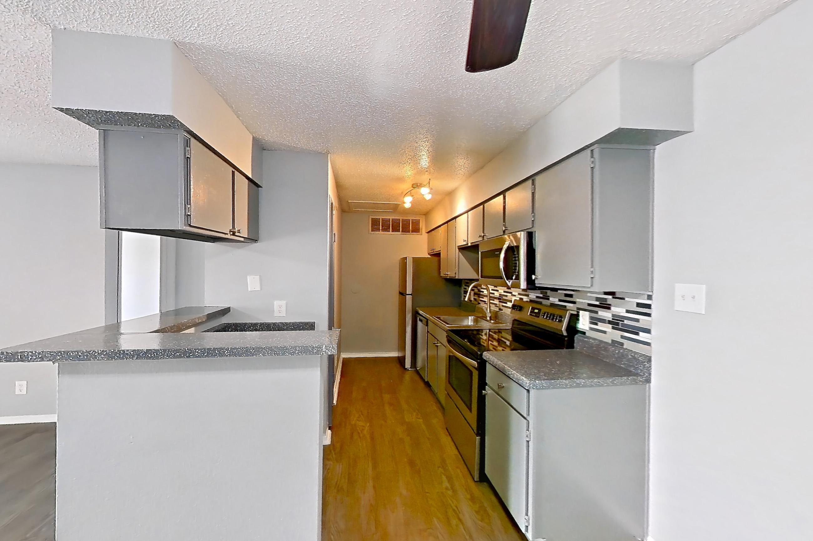Dining room with dark countertops, dark wood-finish flooring, dishwasher, electric range, fireplace, microwave, oven/range, stainless steel appliances, and stone fireplace, Apartment 106 at Marine Creek Apartments