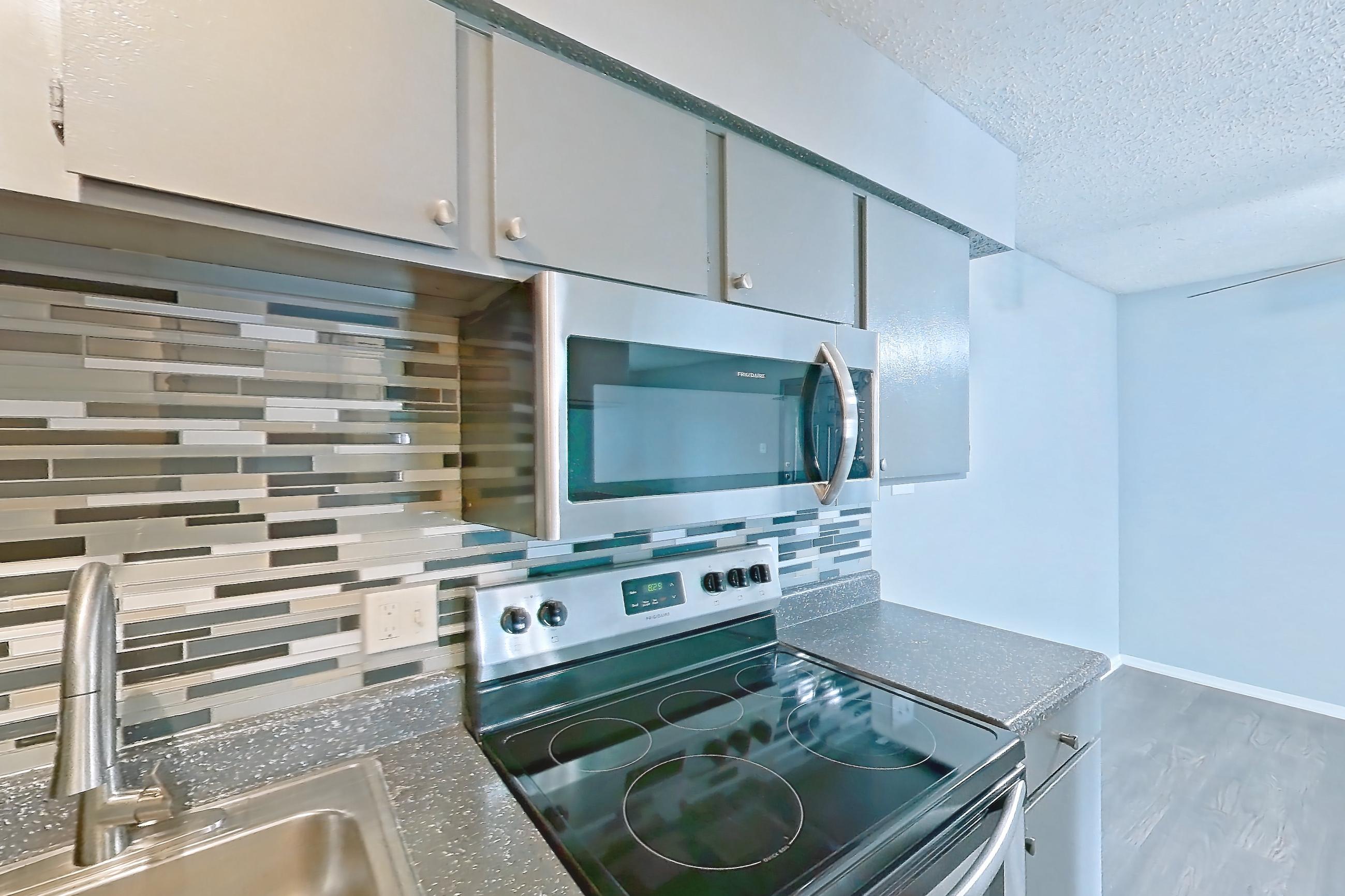 Kitchen with dark countertops, electric range, light countertops, light wood-finish flooring, microwave, oven/range, and stainless steel appliances, Apartment 106 at Marine Creek Apartments