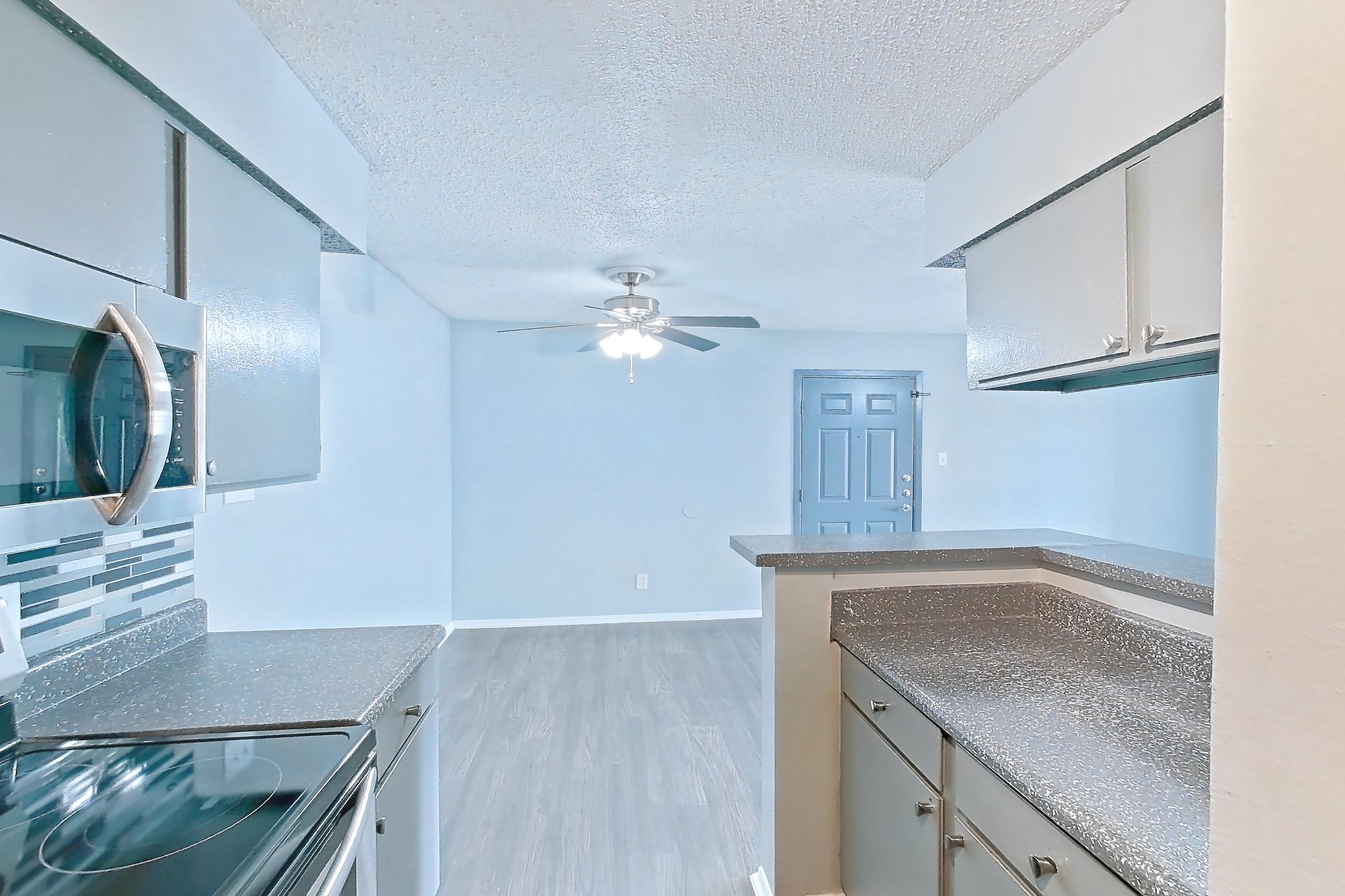 Kitchen with dark countertops, electric range, light countertops, light wood-finish flooring, microwave, oven/range, and stainless steel appliances, Apartment 106 at Marine Creek Apartments