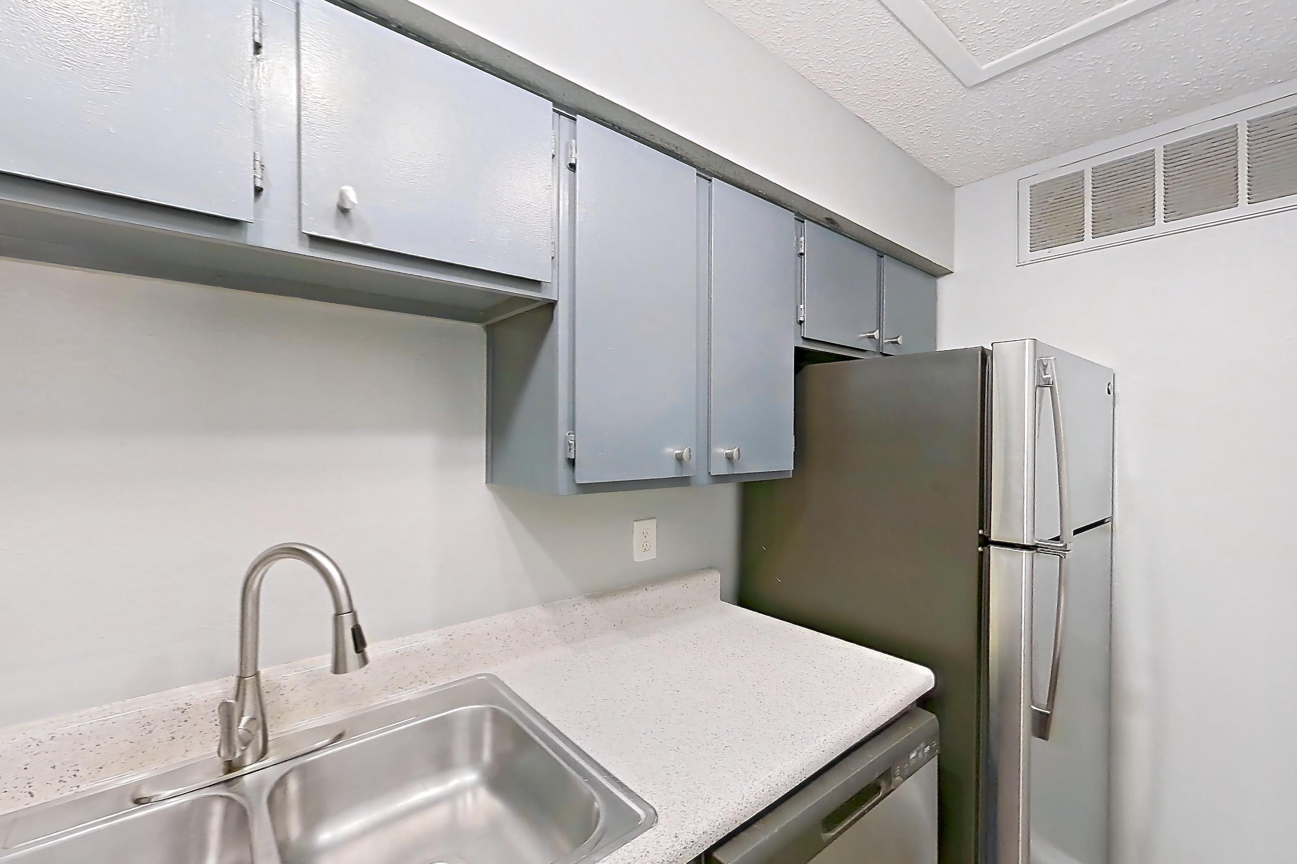 Kitchen with dark wood-finish flooring, dishwasher, electric range, light countertops, light stone countertops, oven/range, range hood, refrigerator, and stainless steel appliances, Apartment 502 at Marine Creek Apartments