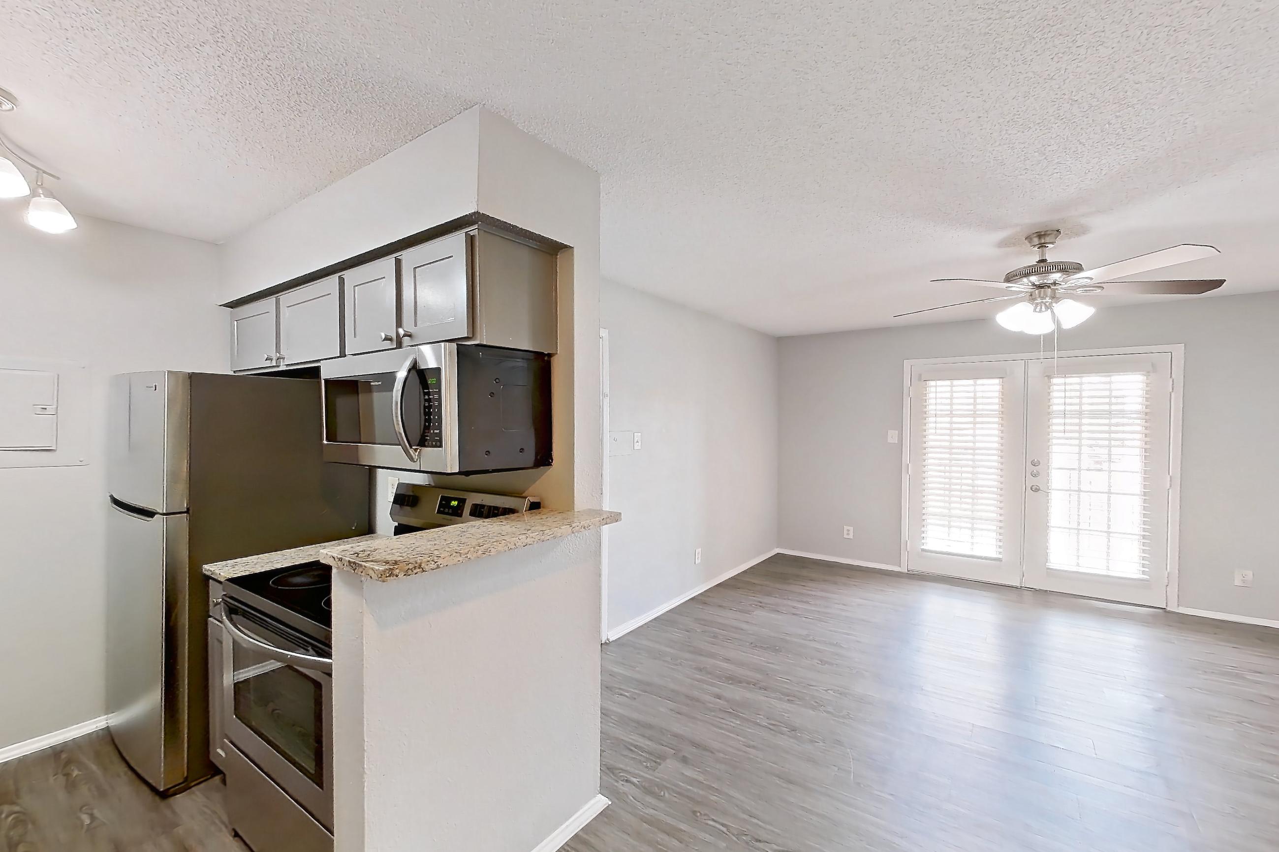 Dining room with electric range, light stone countertops, light wood-finish flooring, microwave, oven/range, refrigerator, and stainless steel appliances, Apartment 608 at Marine Creek Apartments
