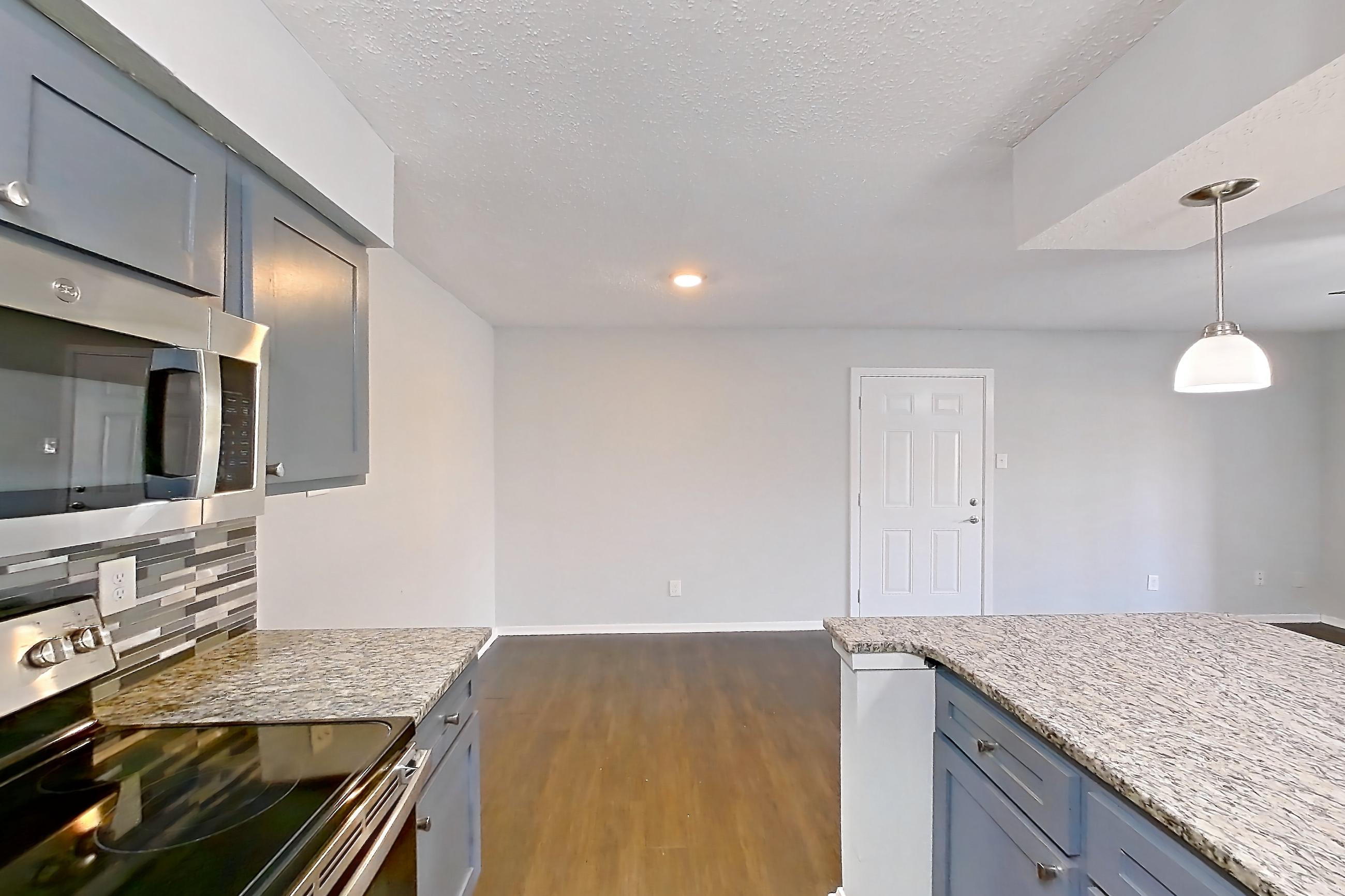 Kitchen with dark wood-finish flooring, electric range, light countertops, light stone countertops, microwave, oven/range, and stainless steel appliances, Apartment 803 at Marine Creek Apartments