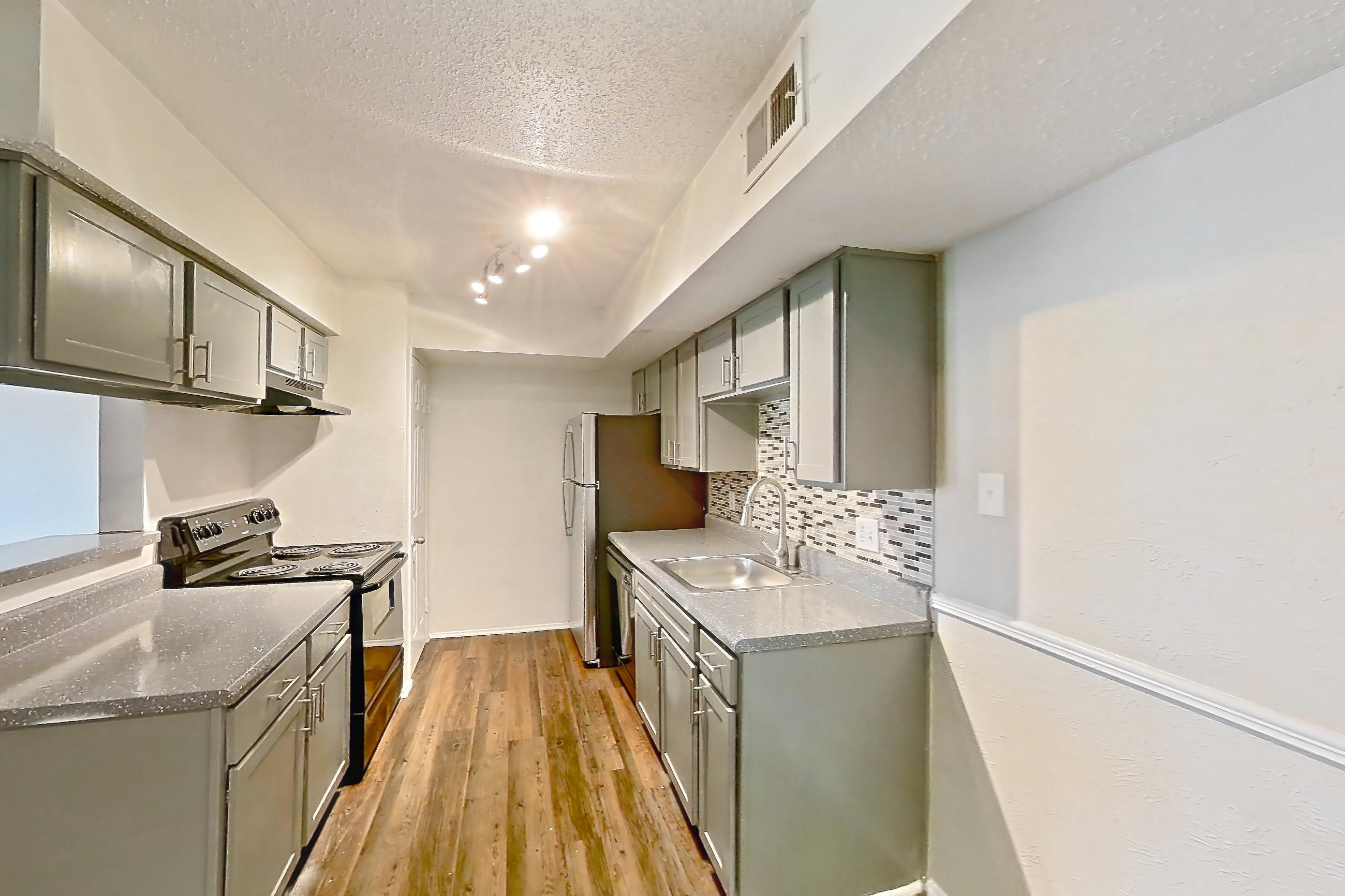Dining room with black appliances, dark countertops, dark wood-finish flooring, dishwasher, electric range, fireplace, light countertops, oven/range, range hood, stainless steel appliances, and stone fireplace, Apartment 902 at Marine Creek Apartments