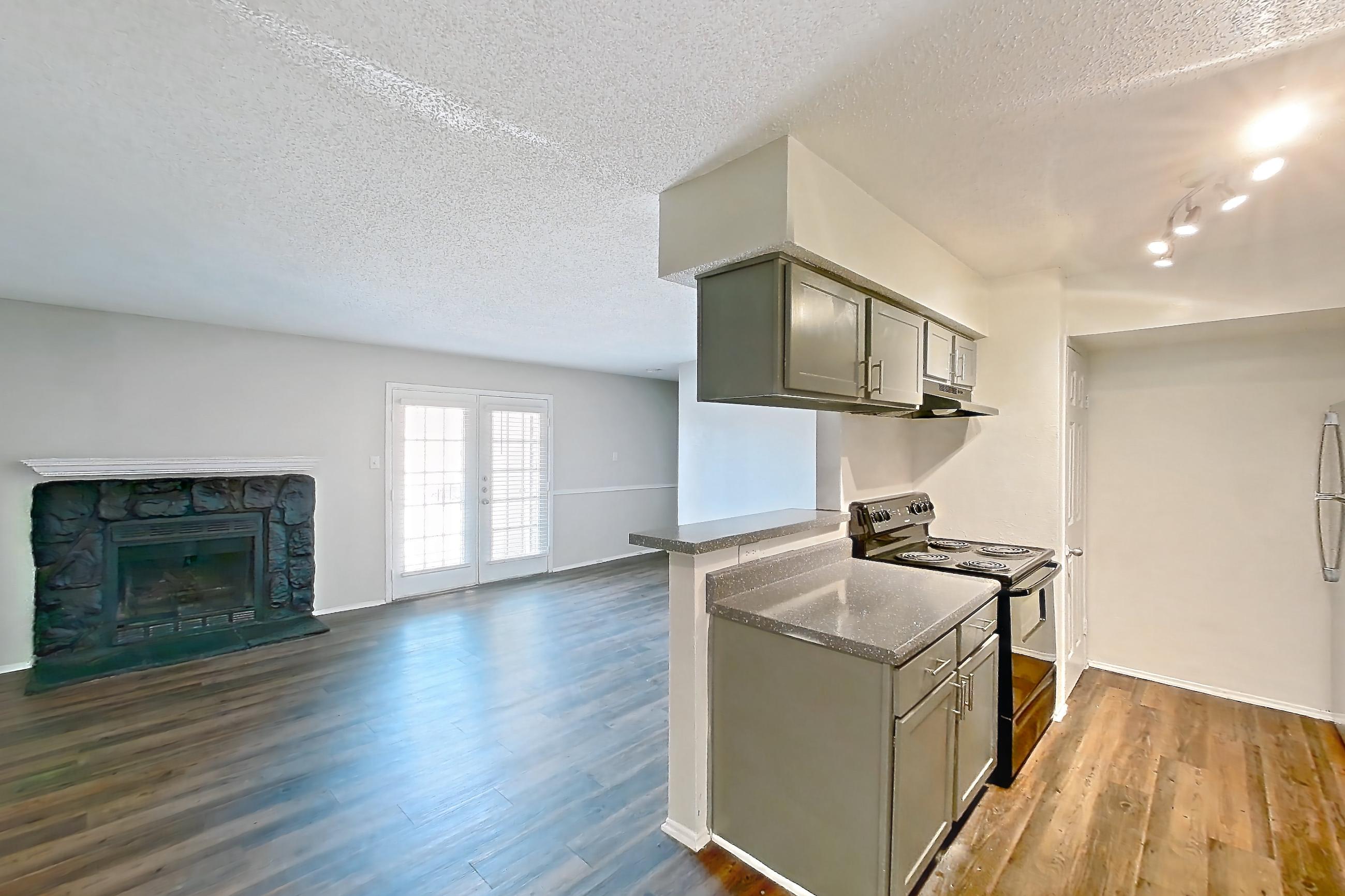 Dining room with black appliances, dark countertops, dark wood-finish flooring, dishwasher, electric range, fireplace, light countertops, oven/range, range hood, stainless steel appliances, and stone fireplace, Apartment 902 at Marine Creek Apartments