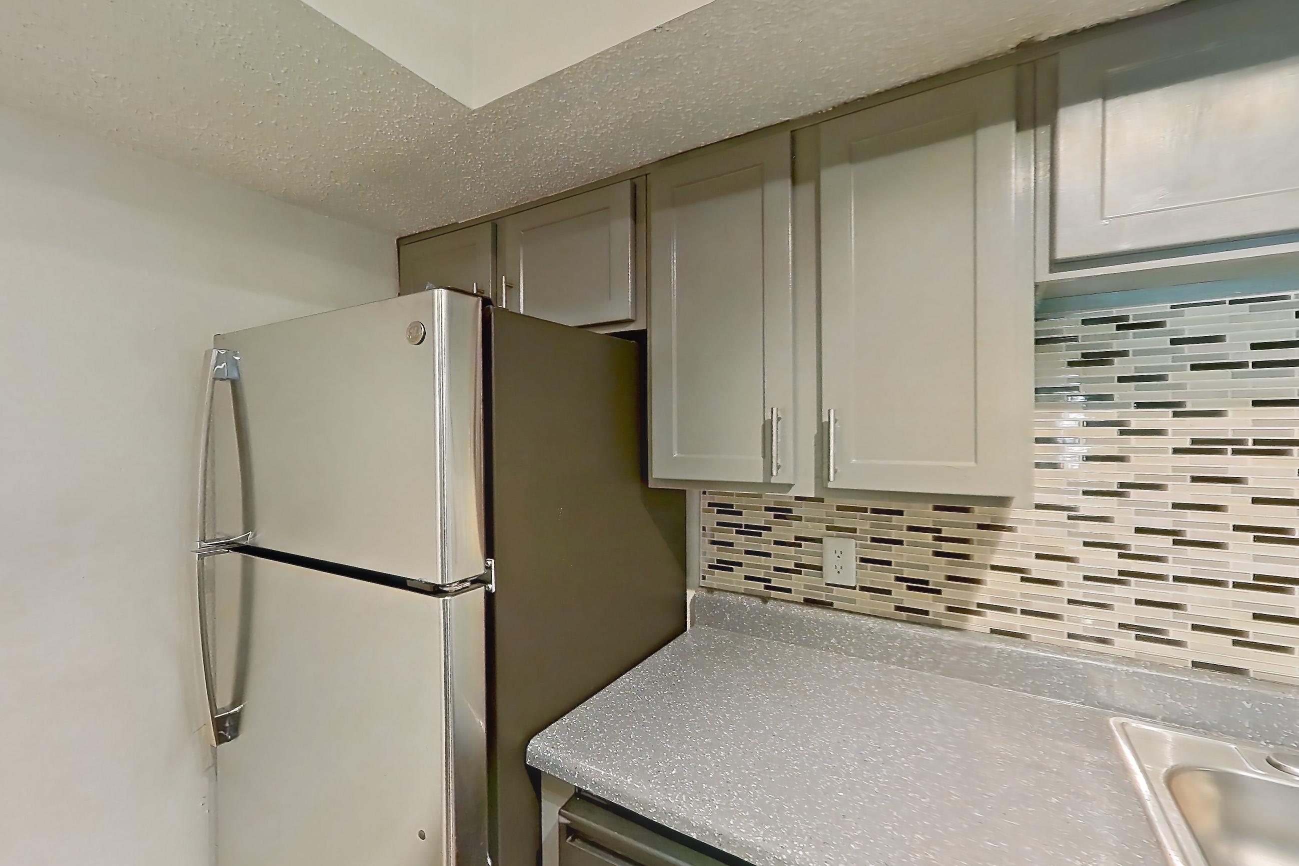 Kitchen with black appliances, dark countertops, dark wood-finish flooring, dishwasher, electric range, light countertops, oven/range, range hood, refrigerator, and stainless steel appliances, Apartment 902 at Marine Creek Apartments